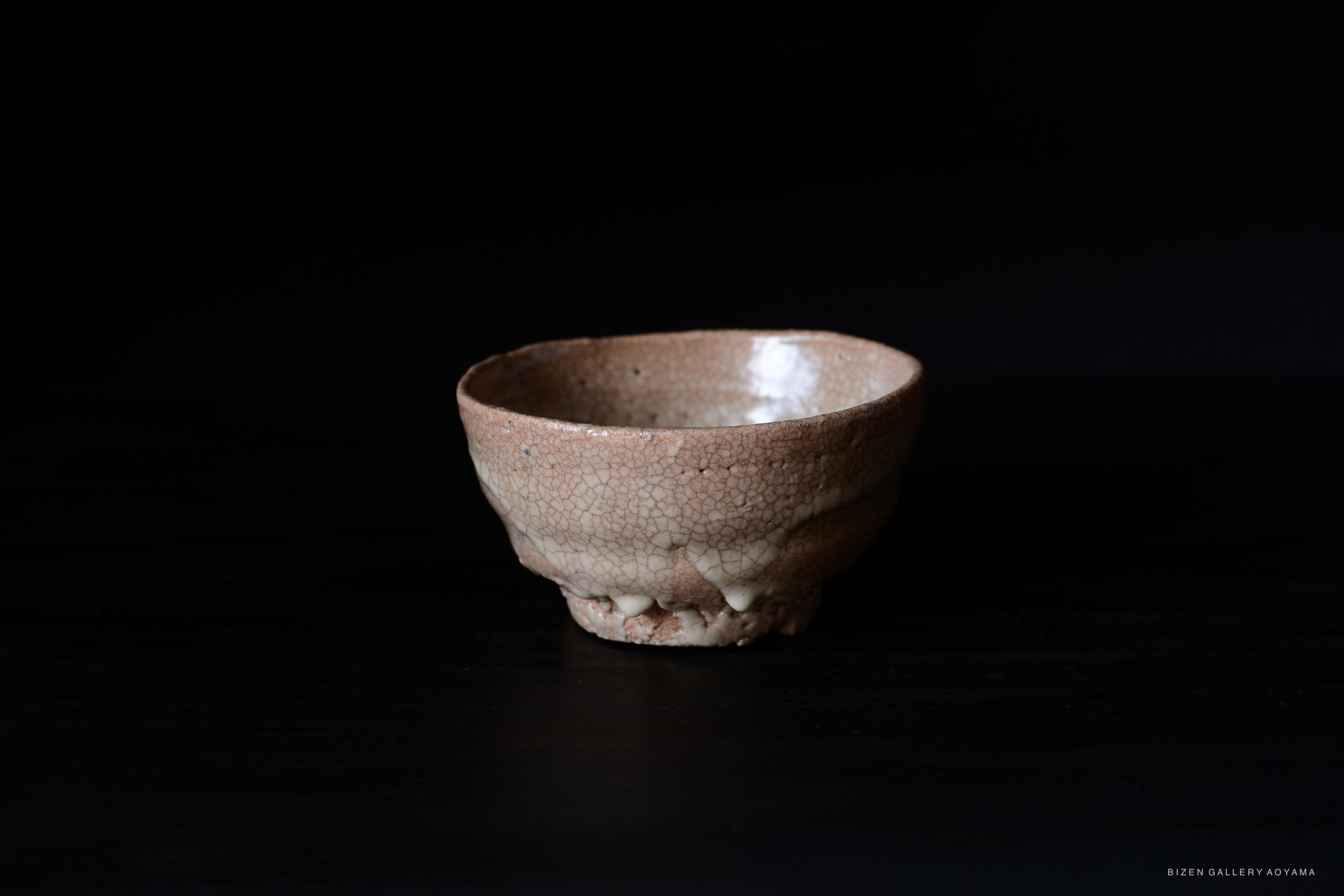 A ceramic bowl with a textured, crackled surface and a soft, warm color against a black background.