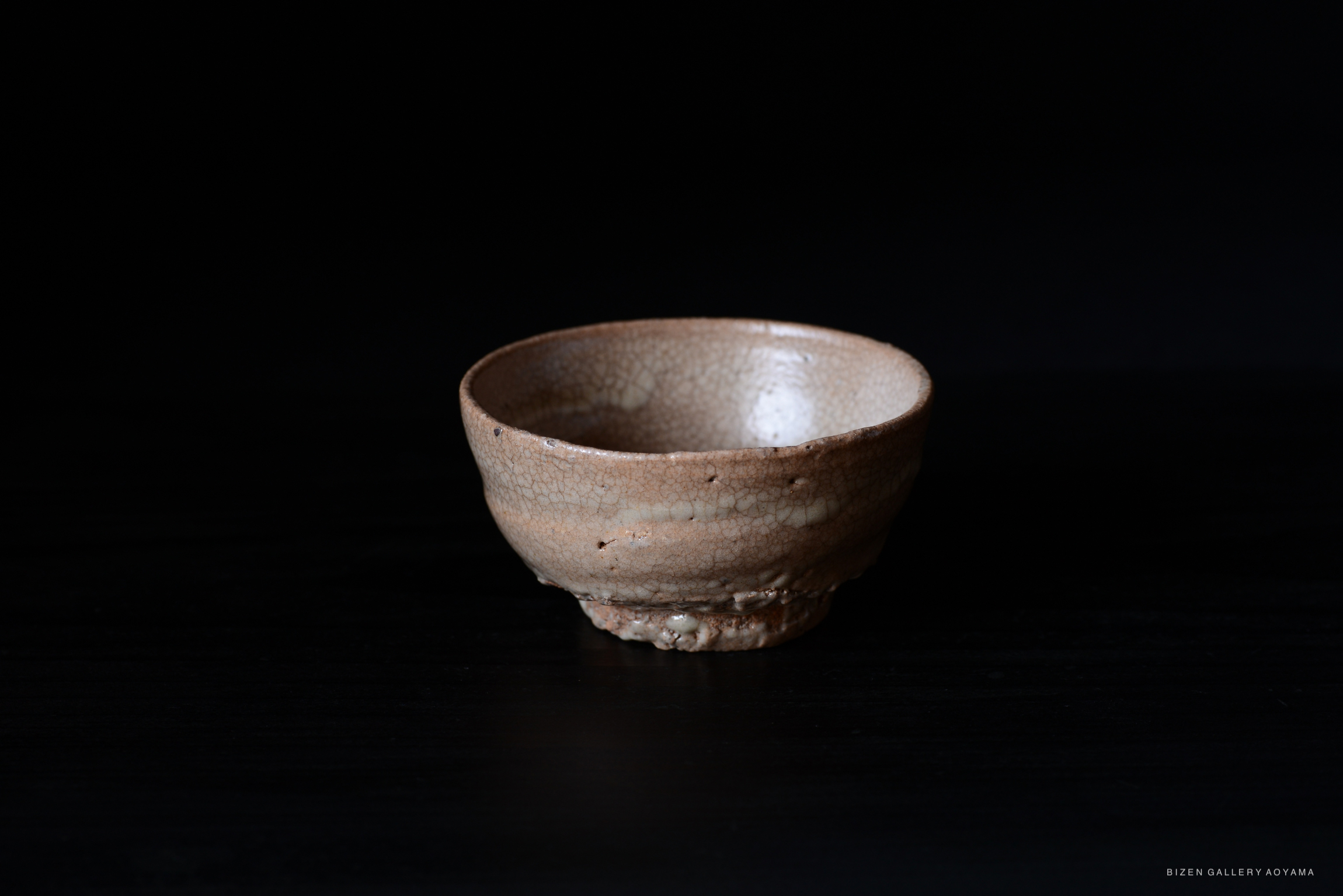 Close-up image of a handcrafted ceramic bowl with a textured surface and subtle cracks, set against a black background.