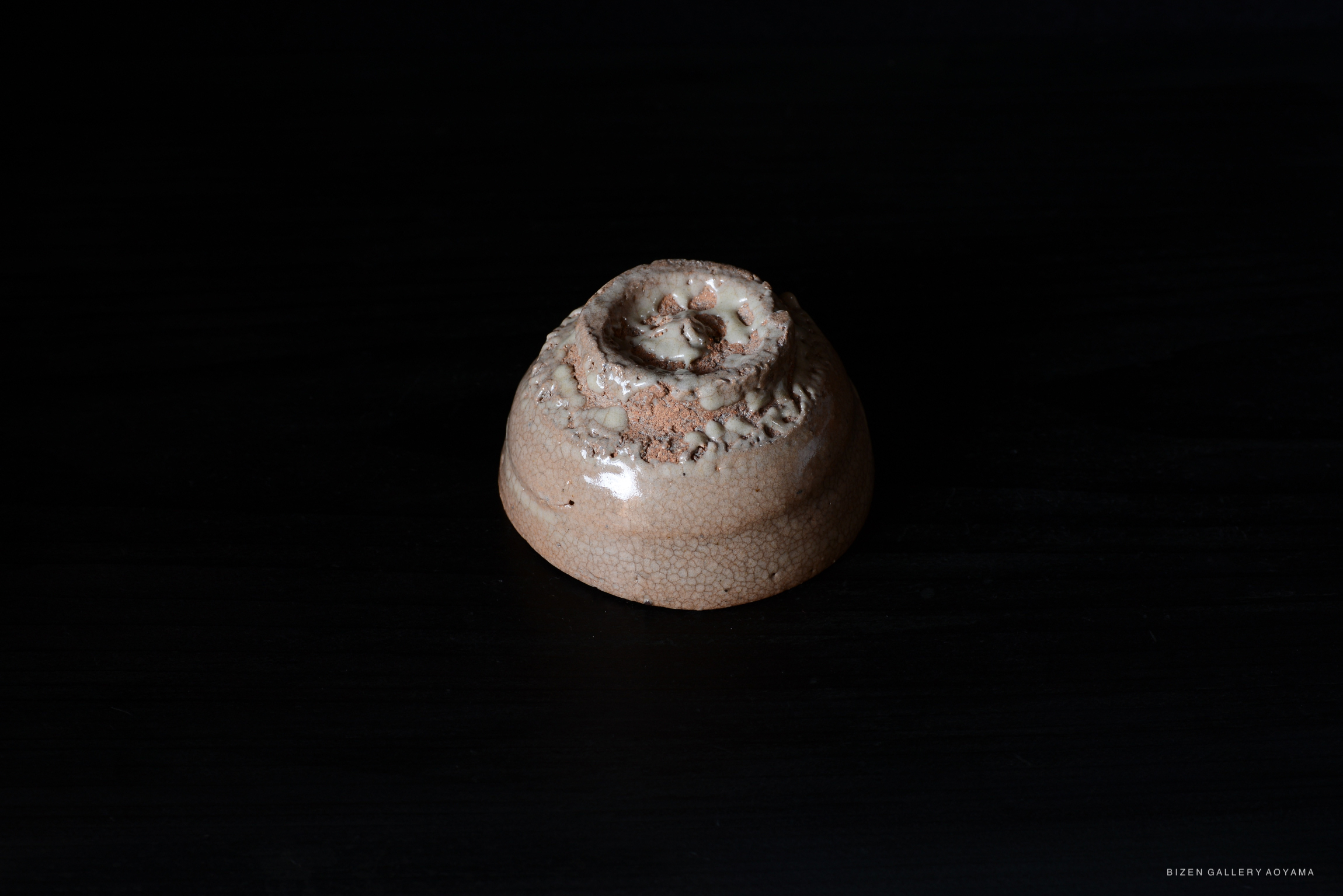 A close-up view of a ceramic piece with a textured surface, showcasing a spiral design and light glaze, set against a dark background.