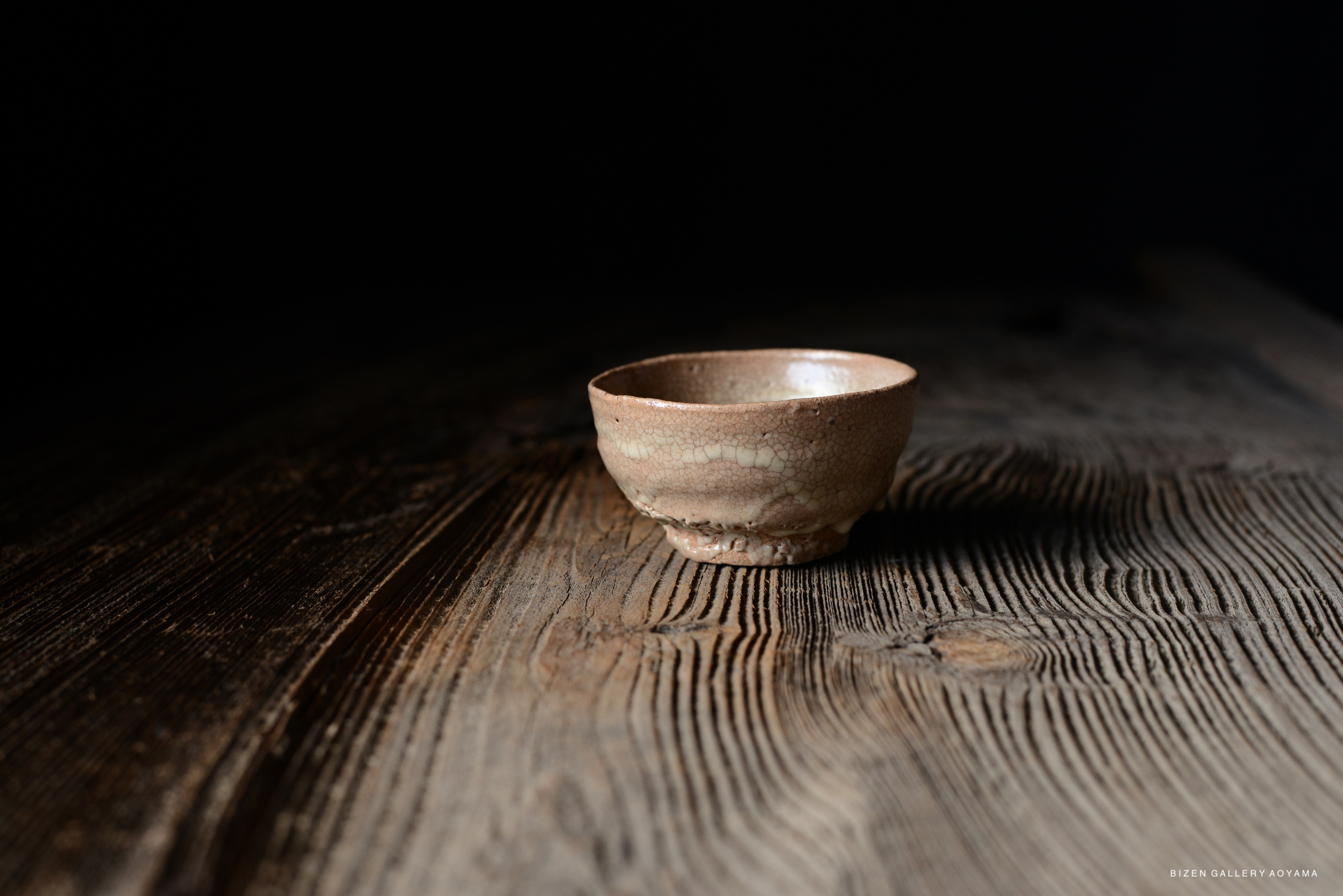 A close-up view of a small, rustic ceramic bowl placed on a wooden surface with visible grain patterns.