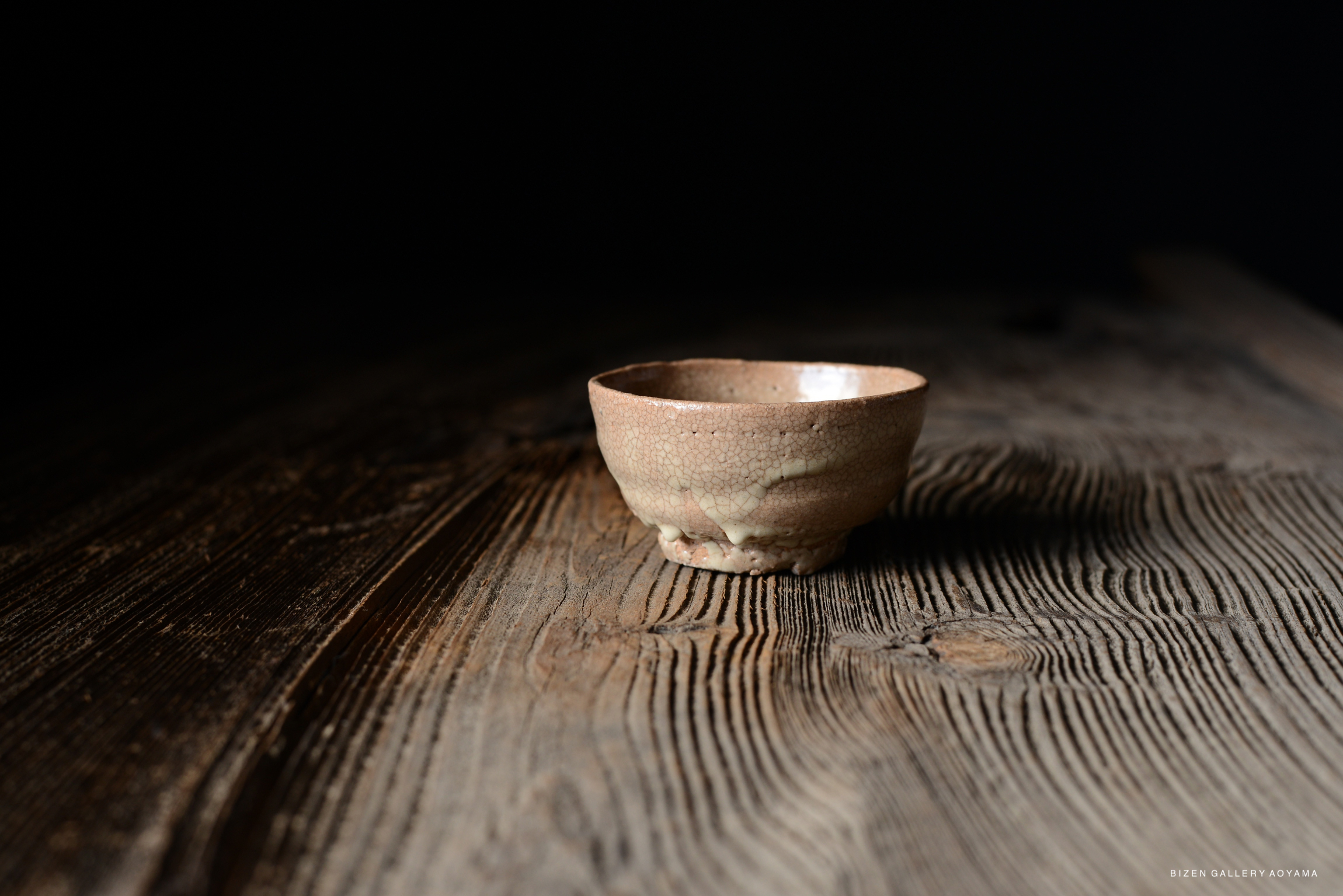 A close-up image of a small, textured ceramic bowl resting on a wooden surface with visible grain patterns, against a dark background.