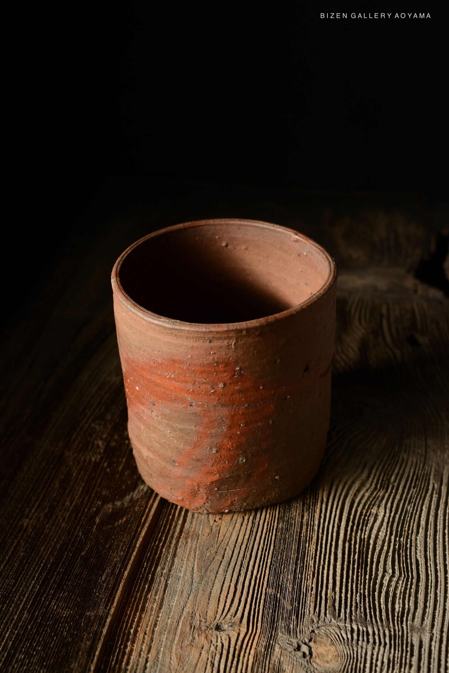 A close-up of a traditional Bizen pottery cup, showcasing its natural terracotta color and texture, placed on a wooden surface.