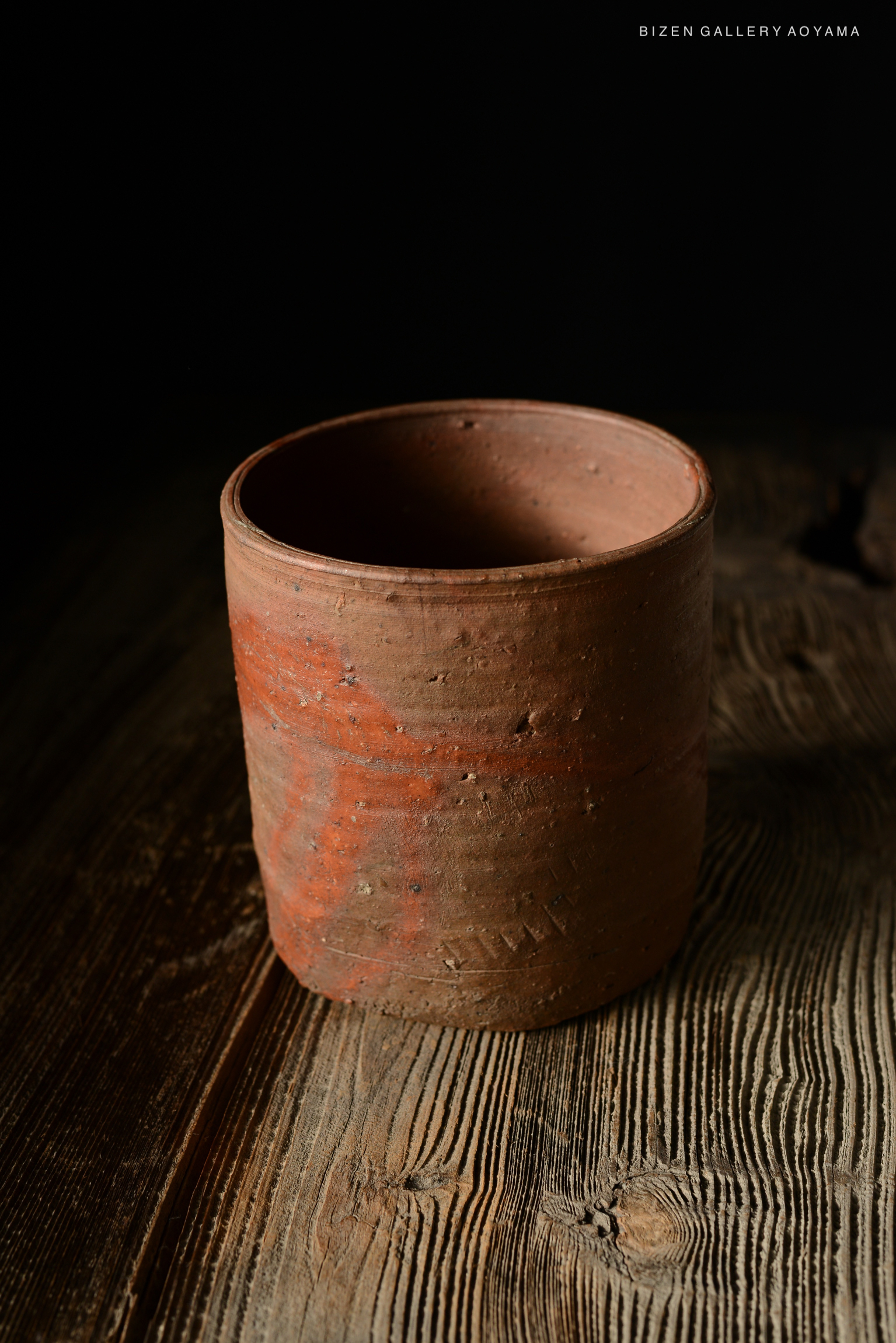 A rustic, handcrafted Bizen pottery cup displayed against a dark background.
