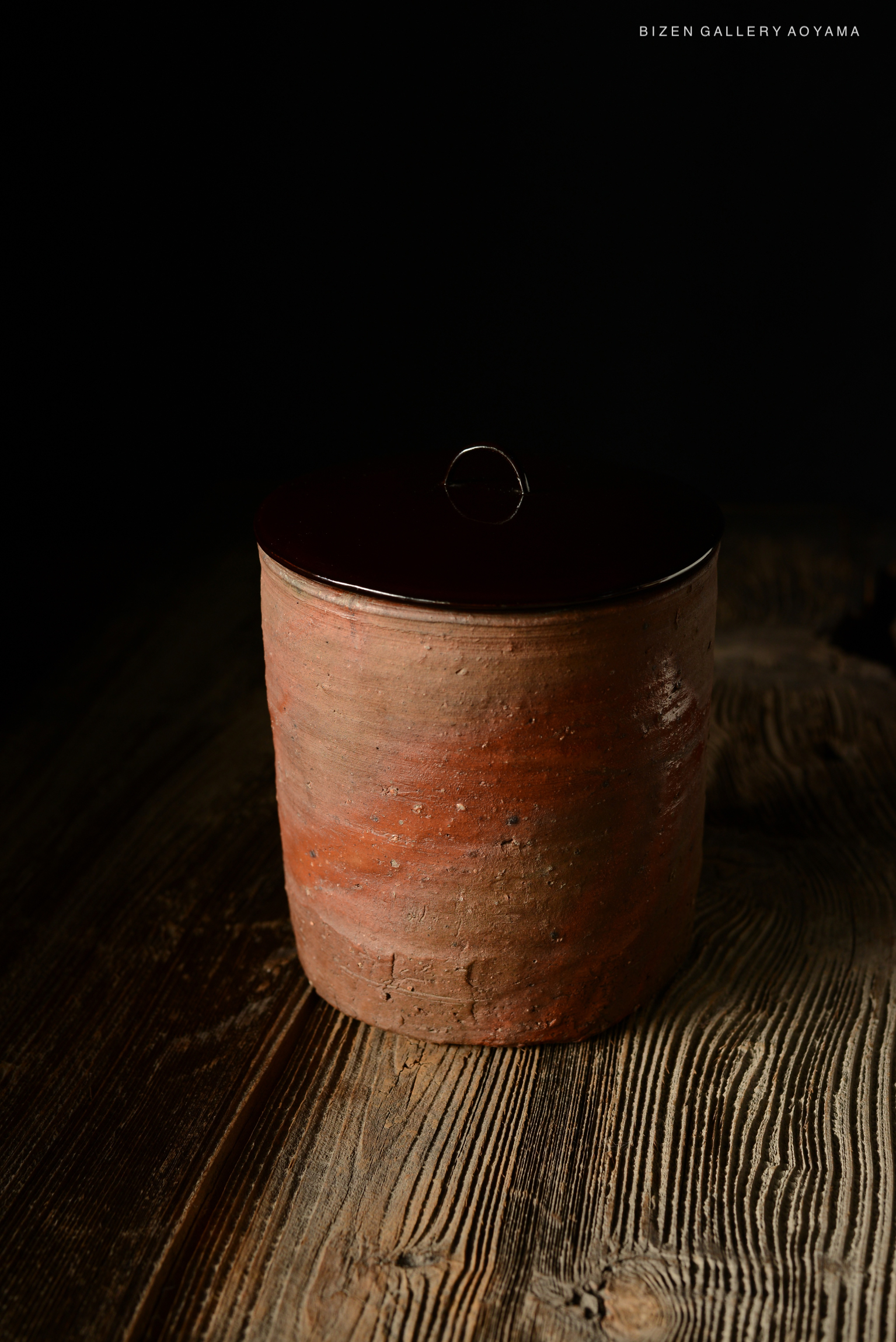 A Bizen Hidasuki Hitoeguchi Mizusashi, a traditional Japanese ceramic water container, displaying a simple yet refined shape, with a dark brown lid and an earthy texture. The piece reflects craftsmanship from the Momoyama to early Edo period.