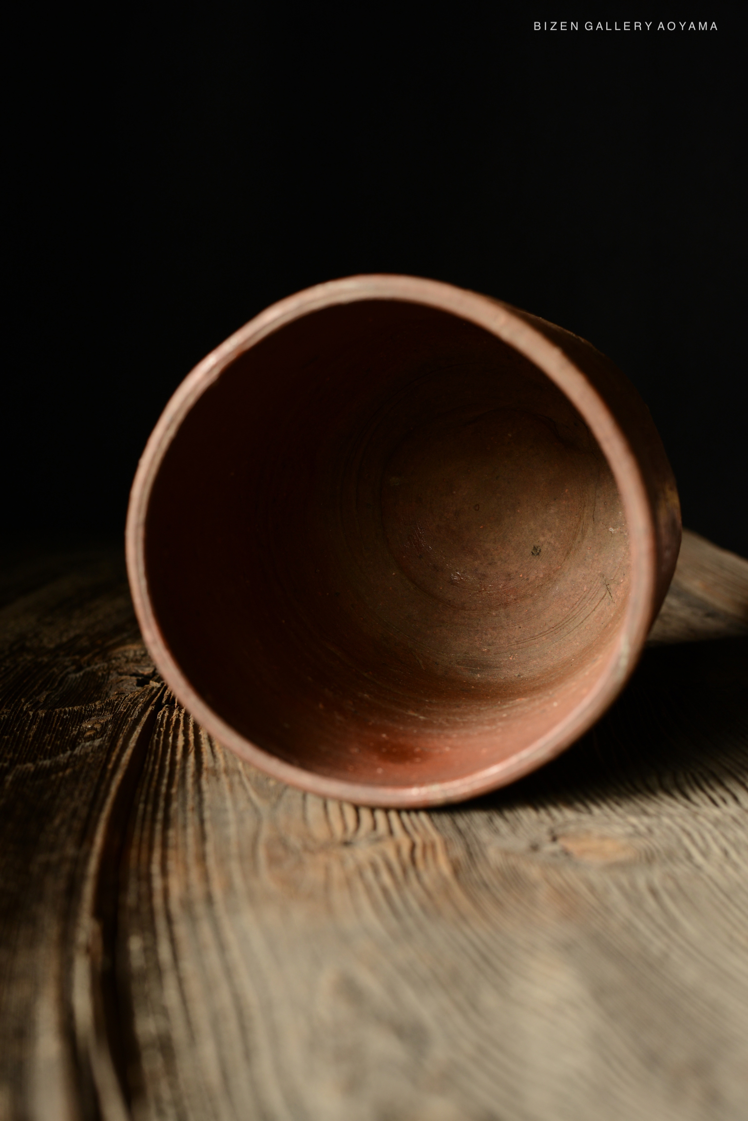 A close-up view of the interior of a Bizen pottery cup, showcasing its earthy texture and warm colors against a dark background.