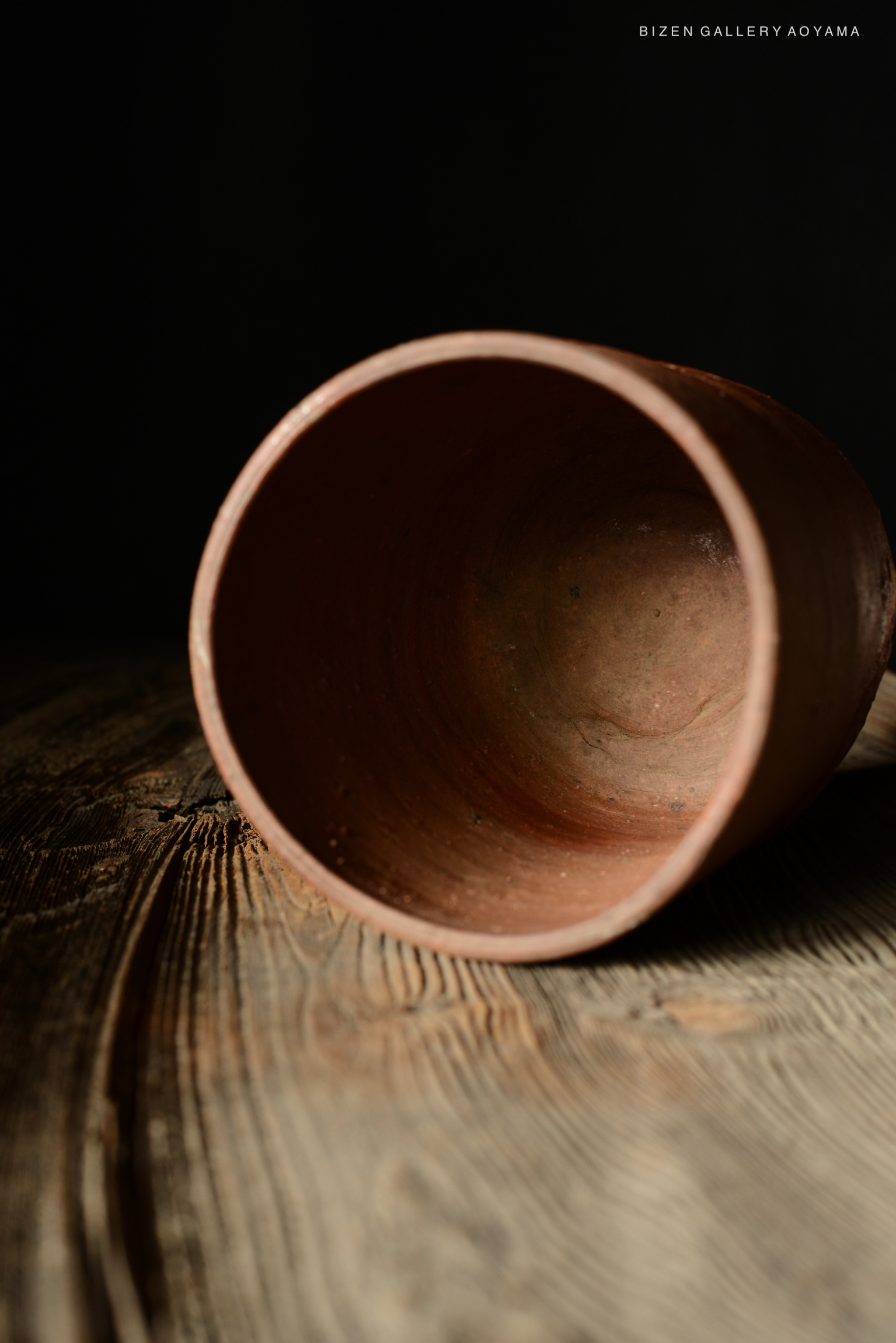 A close-up image of a rustic, unglazed terracotta pot placed on a wooden surface, captured from a slightly tilted angle to showcase its interior.
