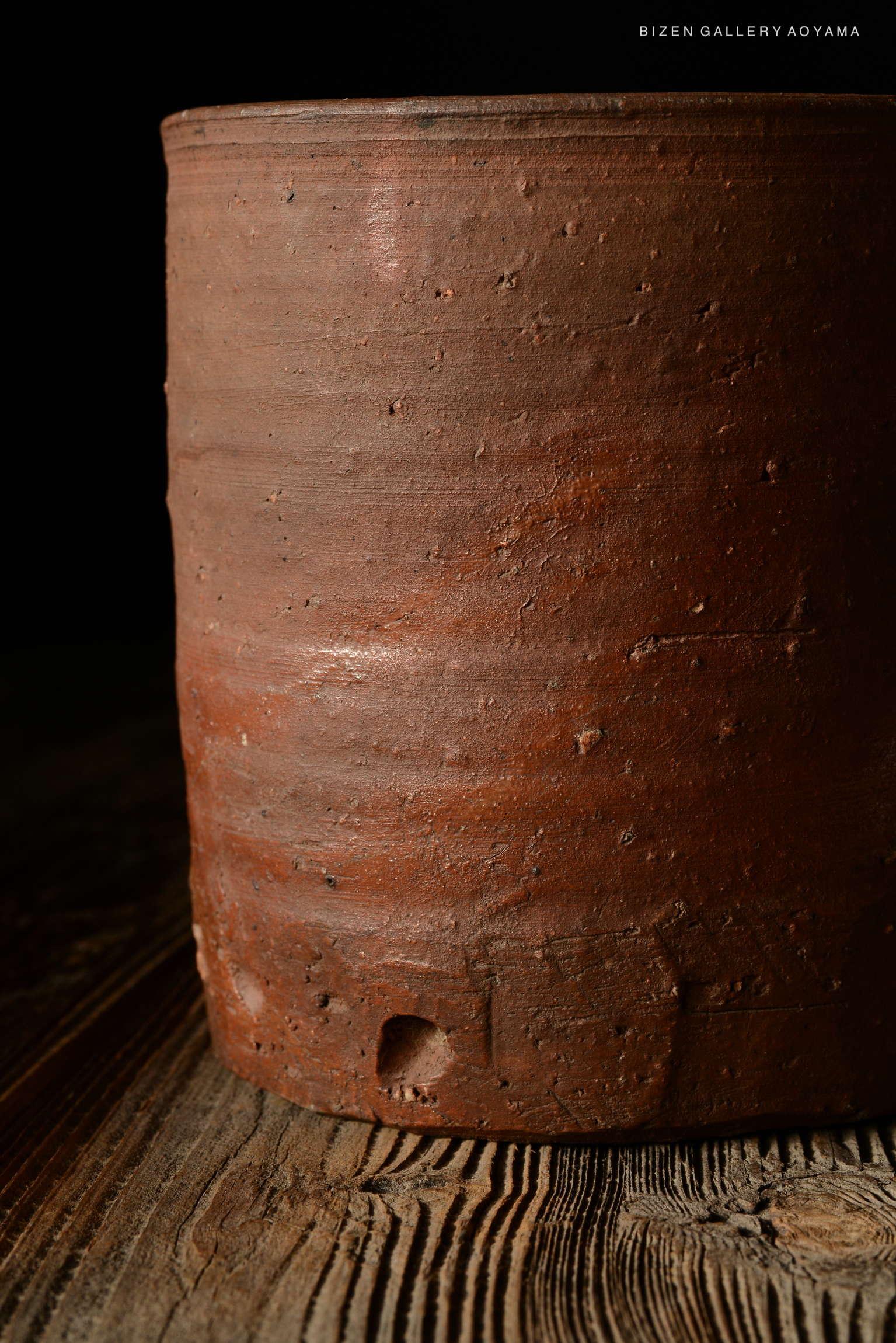 Close-up of a Bizen pottery piece, showcasing its textured surface and earthy color against a dark background.