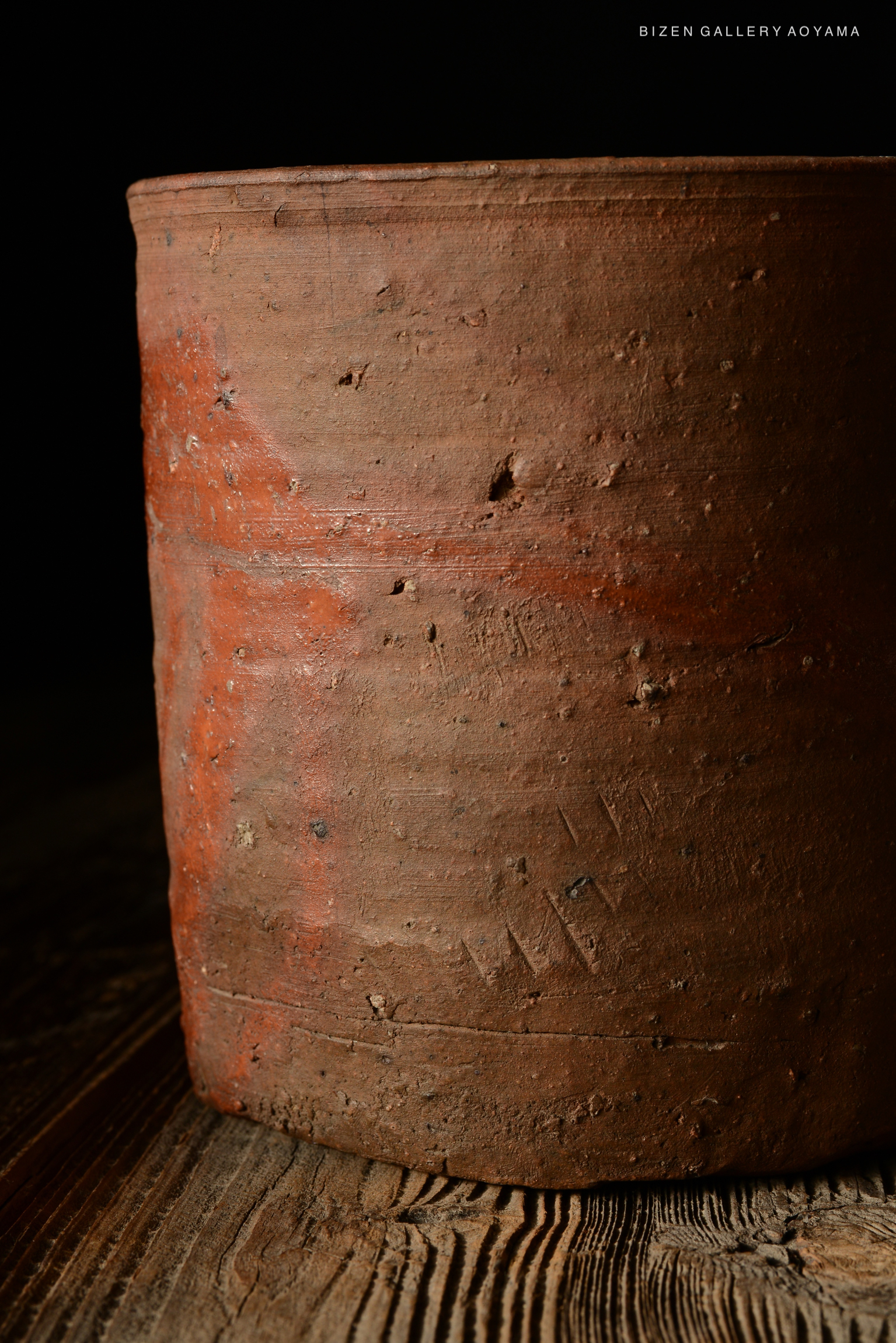Close-up view of a rustic Bizen pottery piece with a textured surface and earthy tones, set against a dark background.