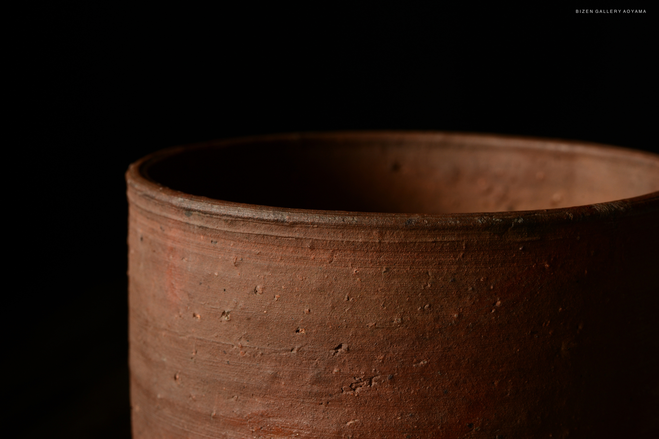 Close-up of a rustic ceramic pot showcasing its textured surface against a dark background.