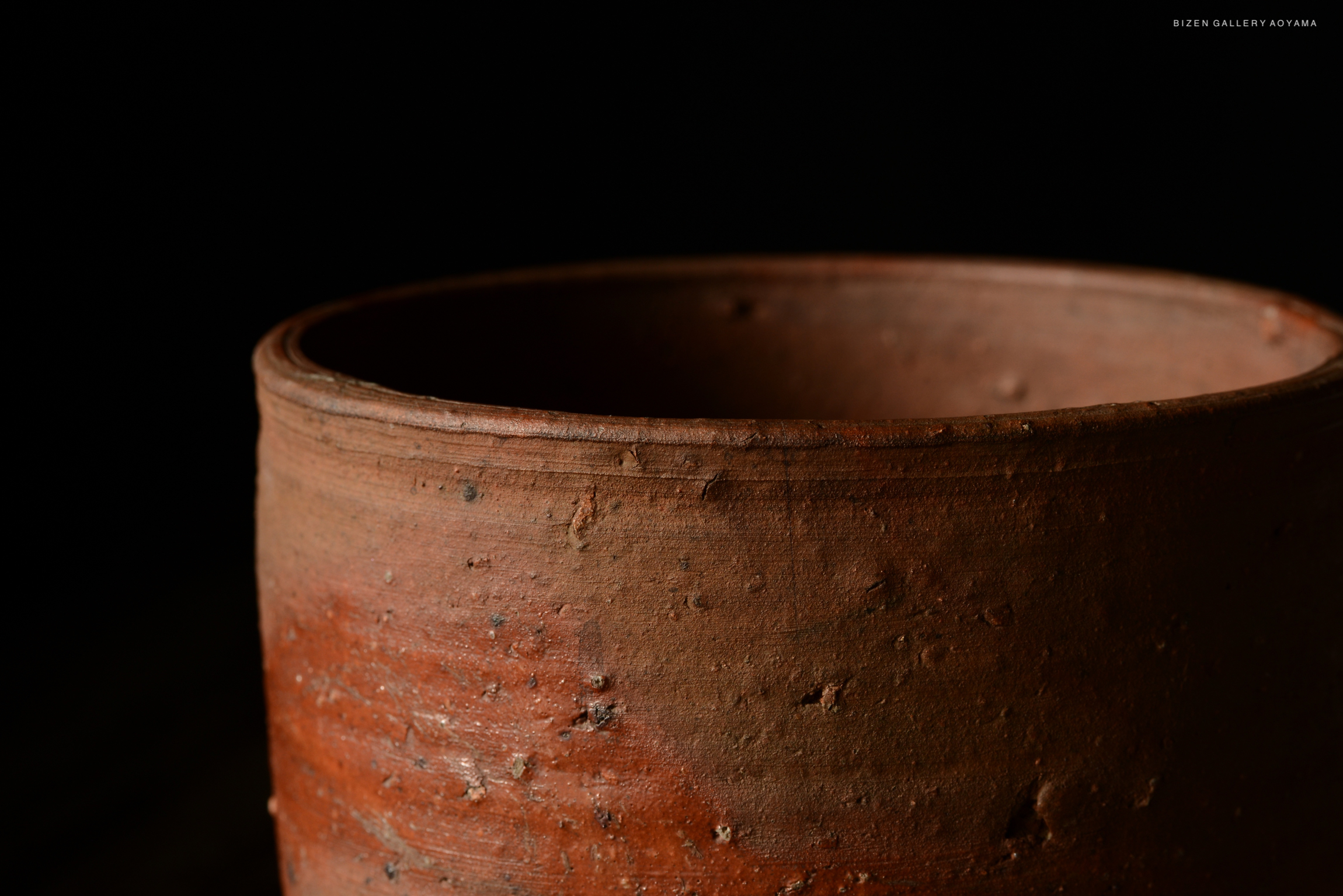 Close-up of a rustic terracotta pot with a textured surface against a dark background.