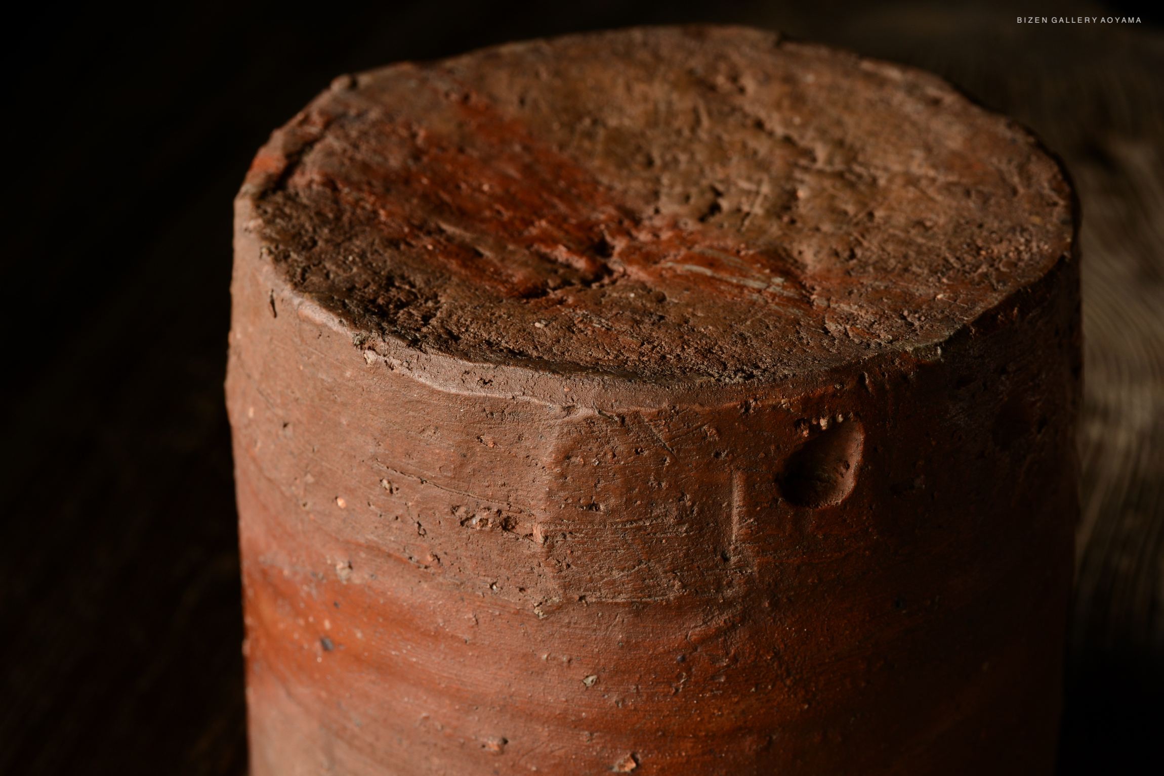 Close-up view of a round, textured clay pot with a rustic surface and earthy color.