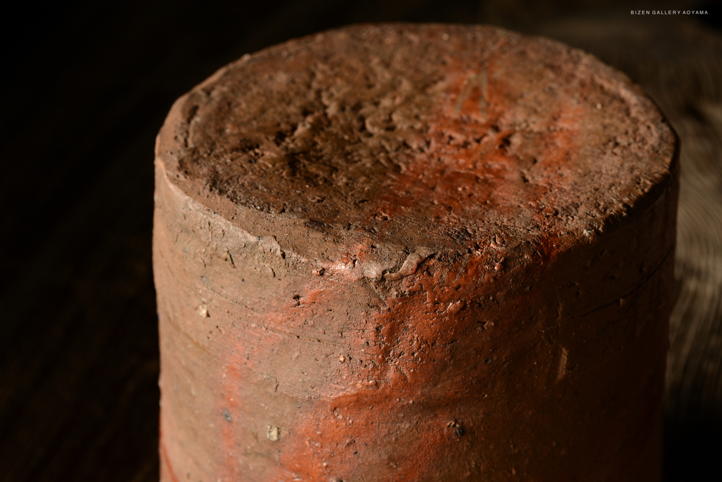 Close-up of a round, textured clay pot with a rough surface and earthy tones, set against a dark background.