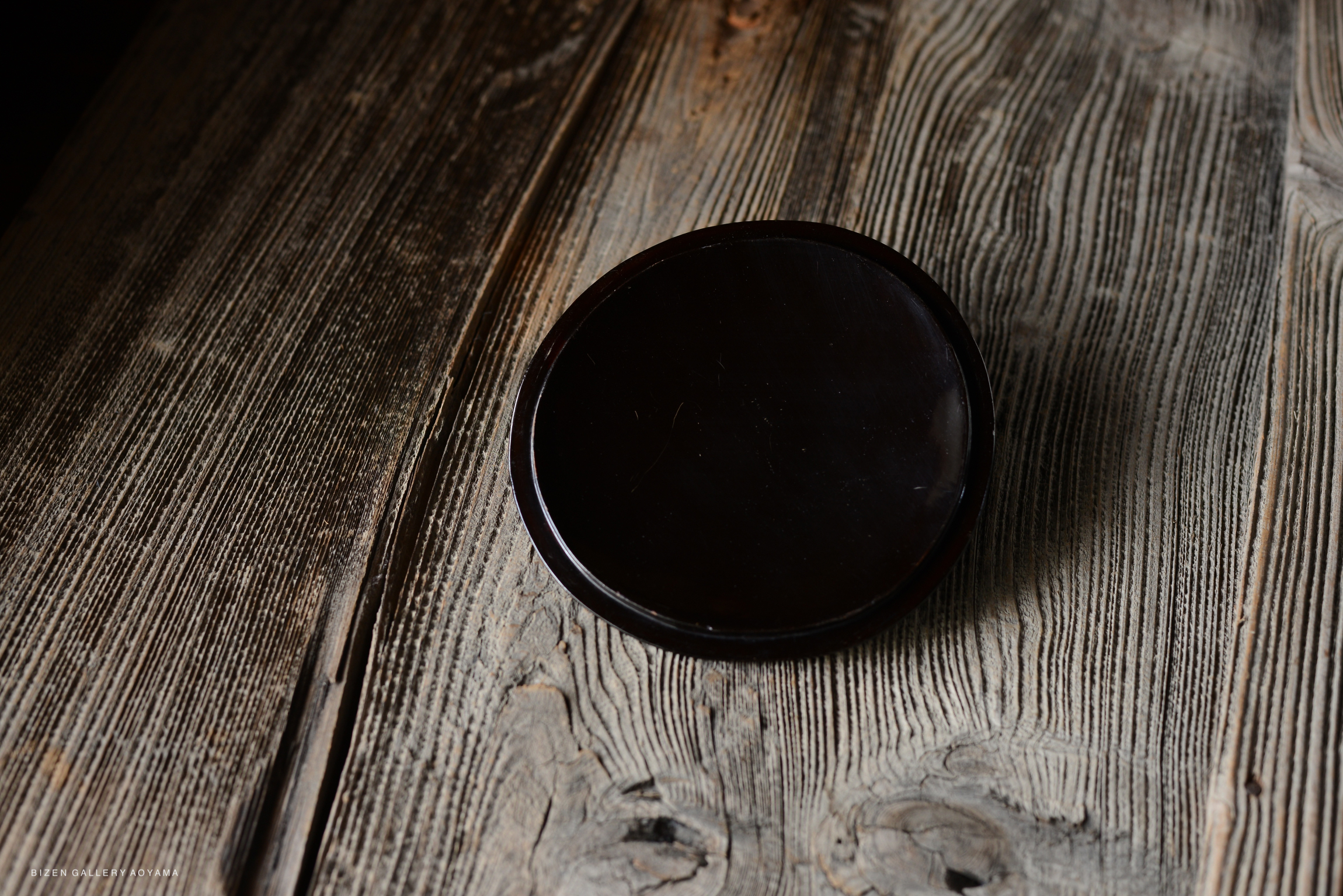 Close-up of a dark, round ceramic object placed on a textured wooden surface, highlighting its smooth finish and simple design.