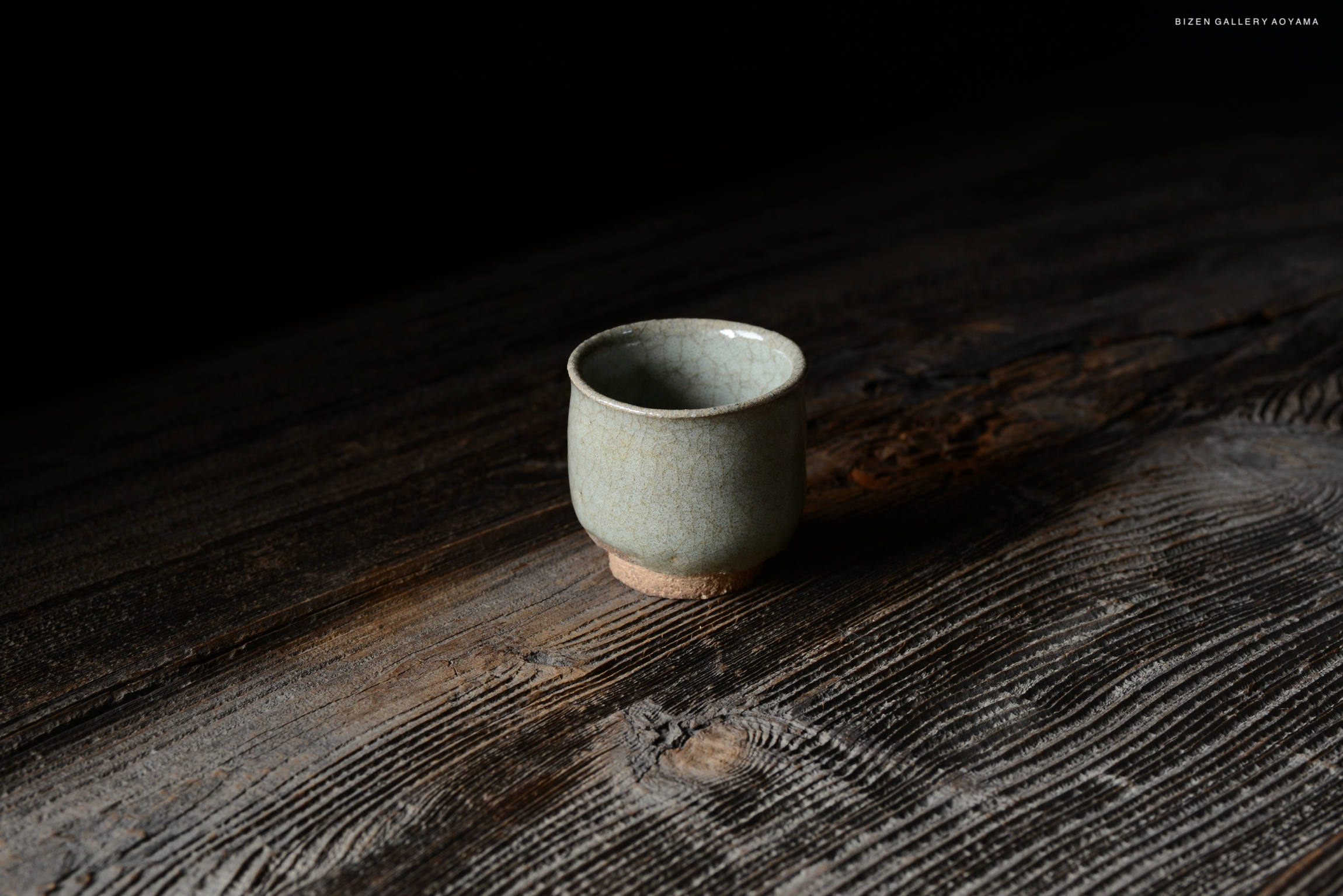 A small, light green ceramic cup positioned on a dark wooden surface, showcasing its textured exterior and a plain base.