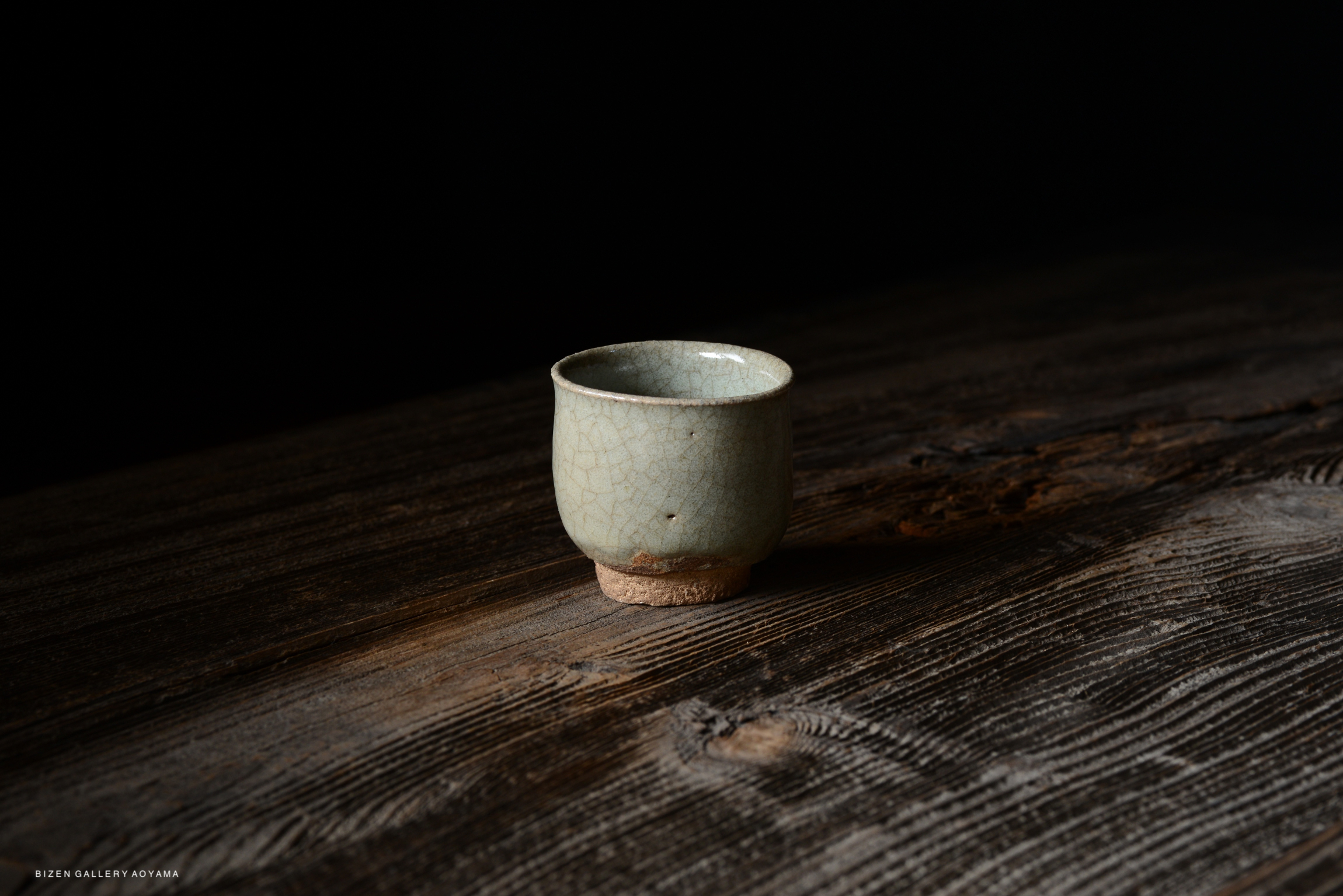 A small, light green ceramic cup with a slightly textured surface, sitting on a dark wooden table.