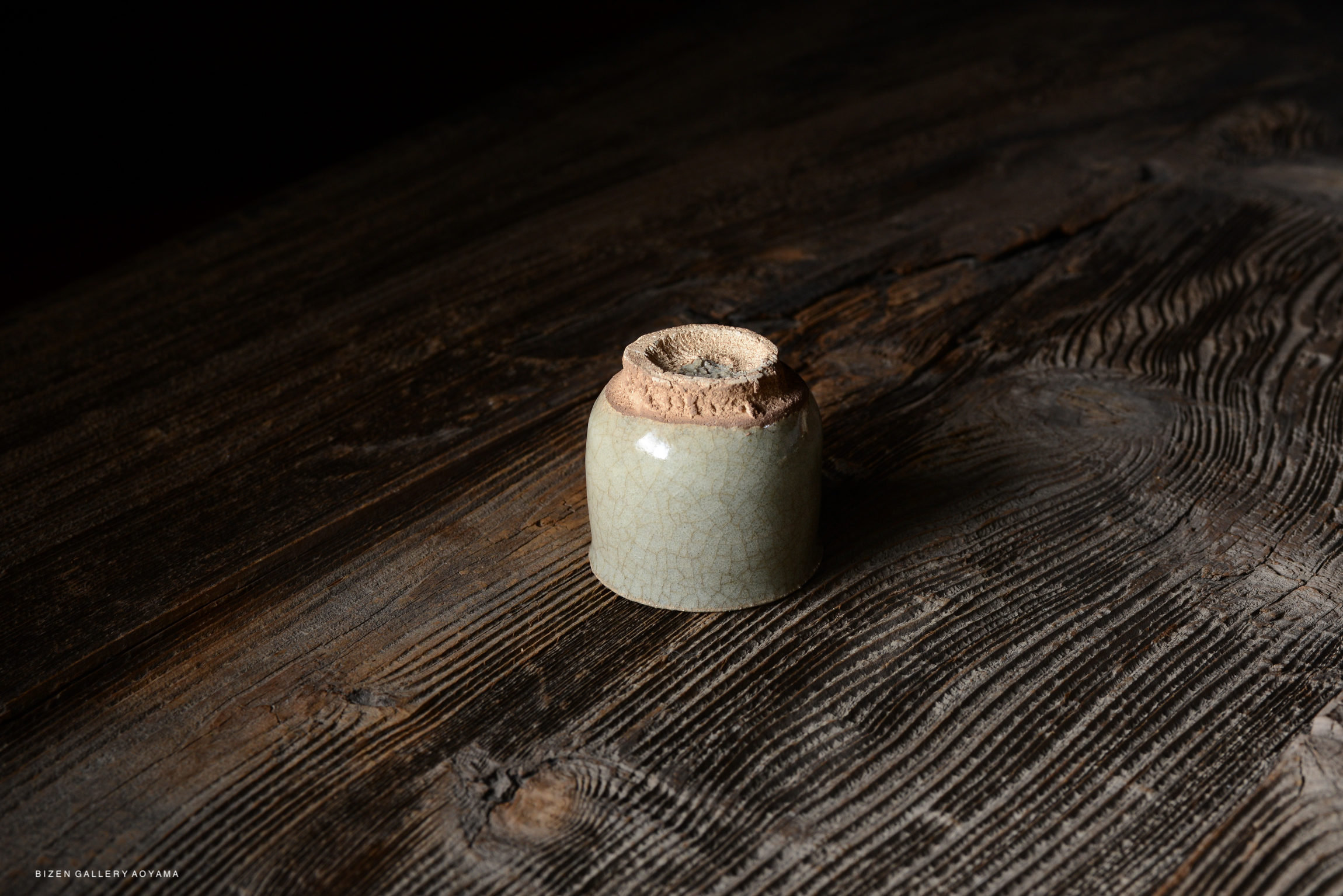 A close-up view of a small, cracked-glazed ceramic vase resting on a dark wooden surface.