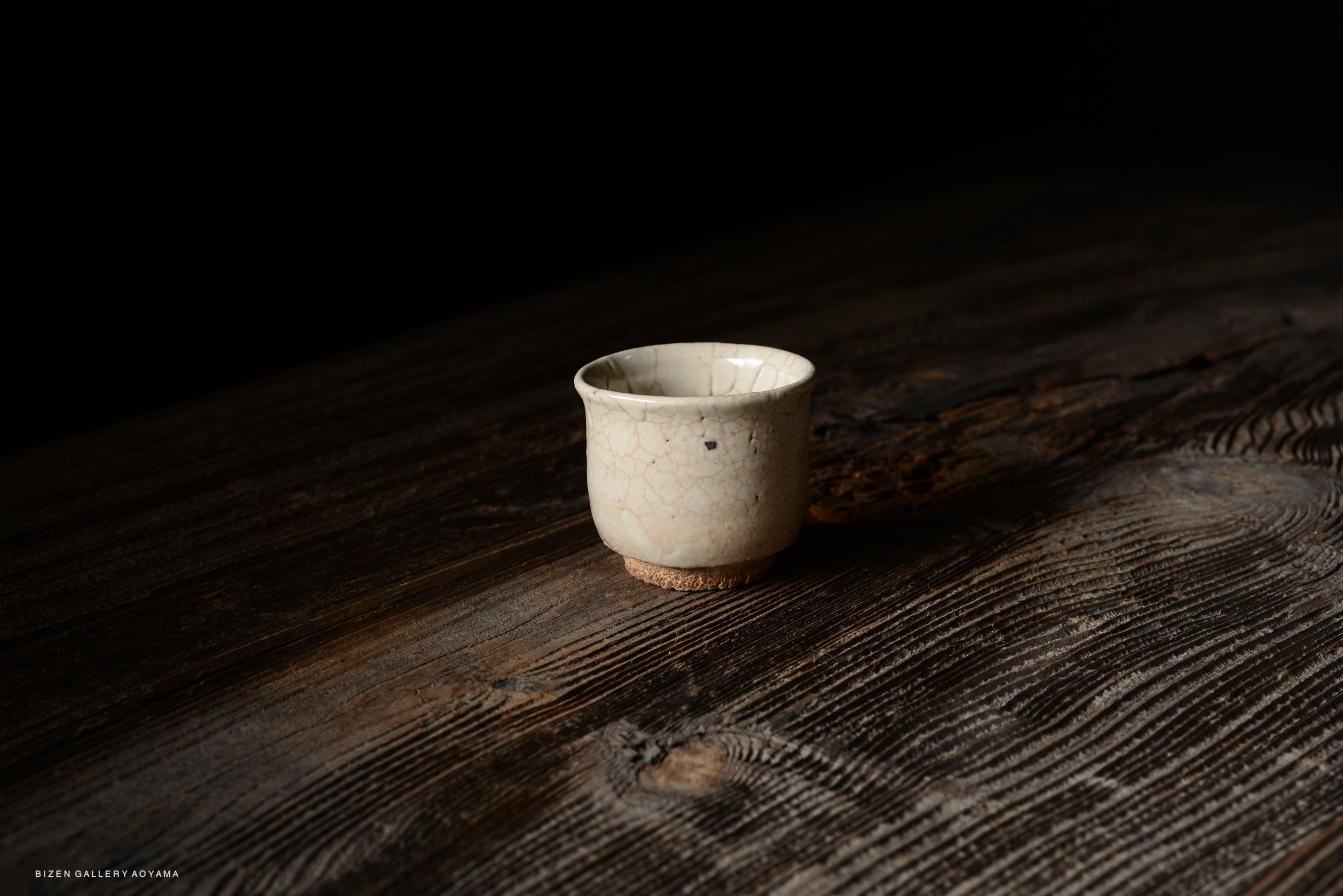 A small cracked ceramic cup placed on a wooden surface against a dark background.