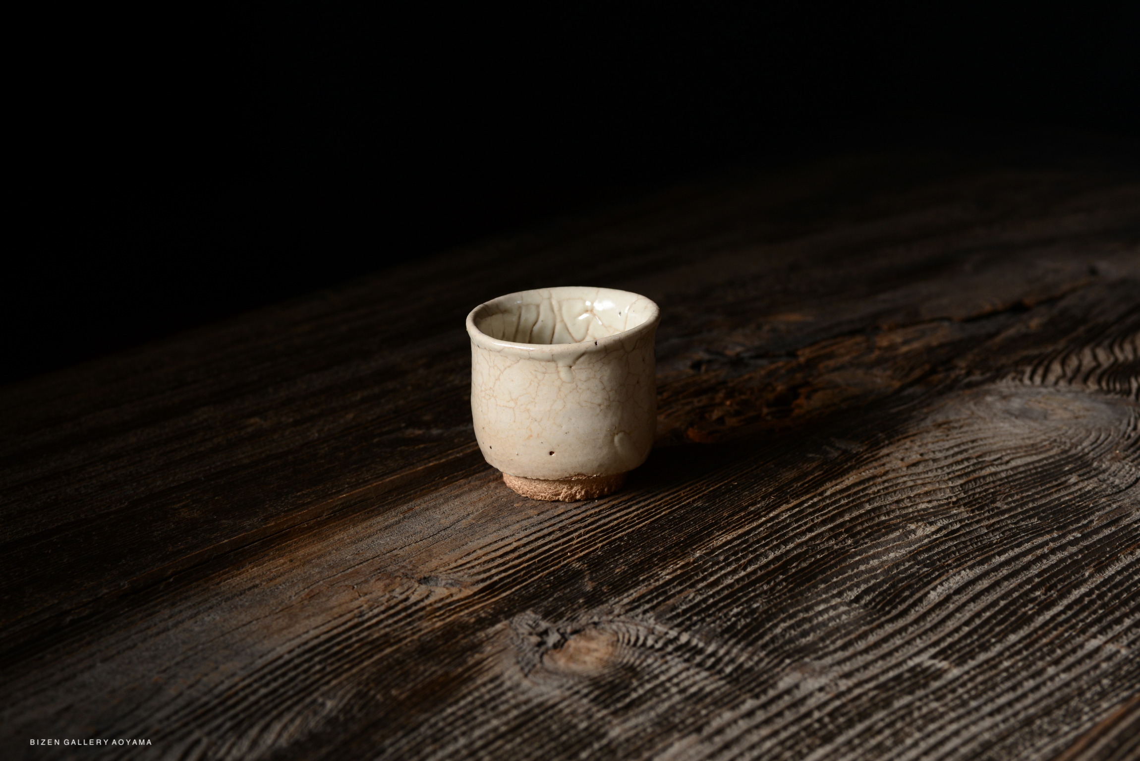 A small, cracked ceramic cup positioned on a rustic wooden table, with a dark background.
