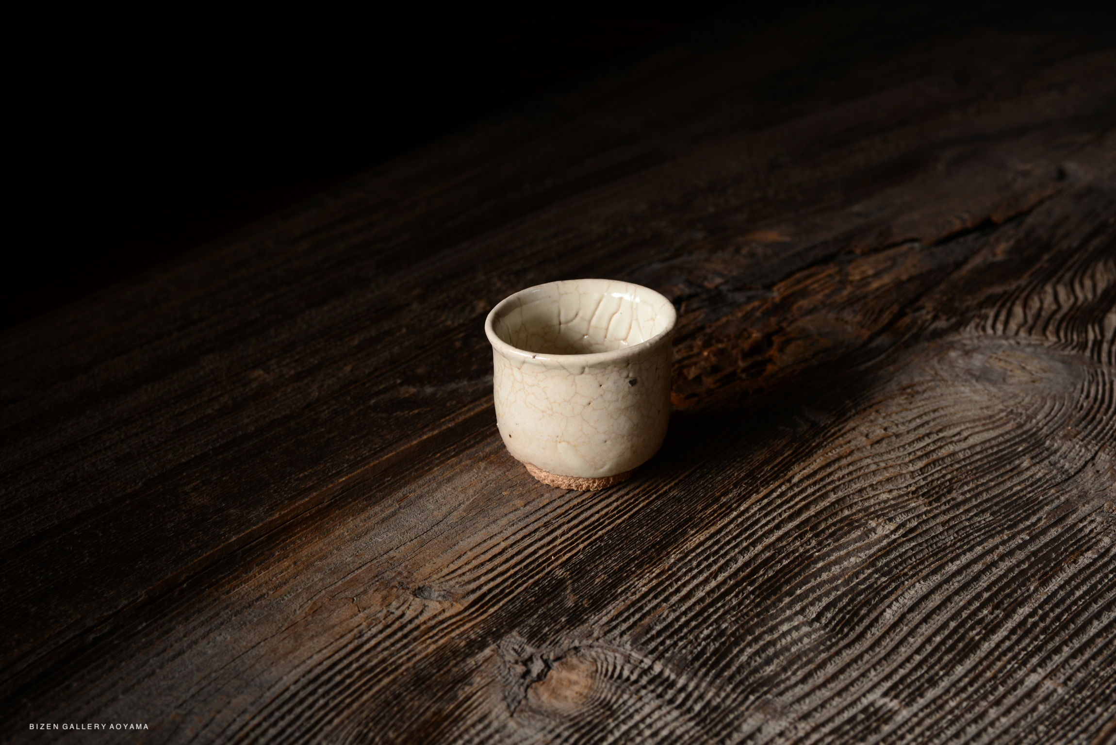 A close-up image of a small, cracked ceramic cup resting on a textured wooden surface.