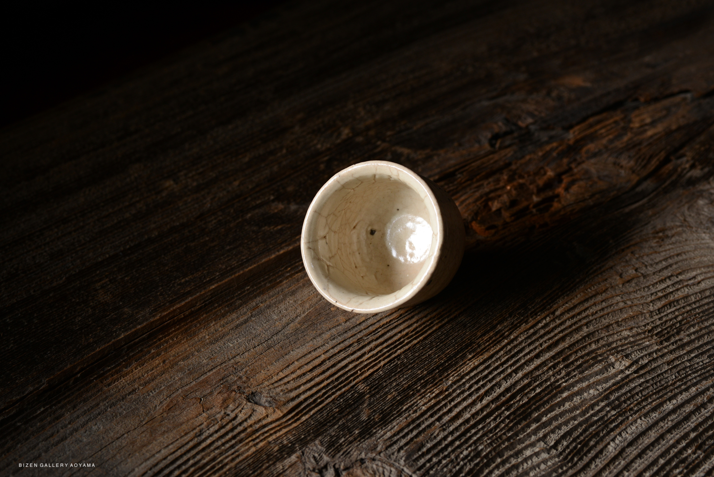 A small, white ceramic bowl sitting on a rustic wooden surface, featuring a glossy interior and a cracked exterior.