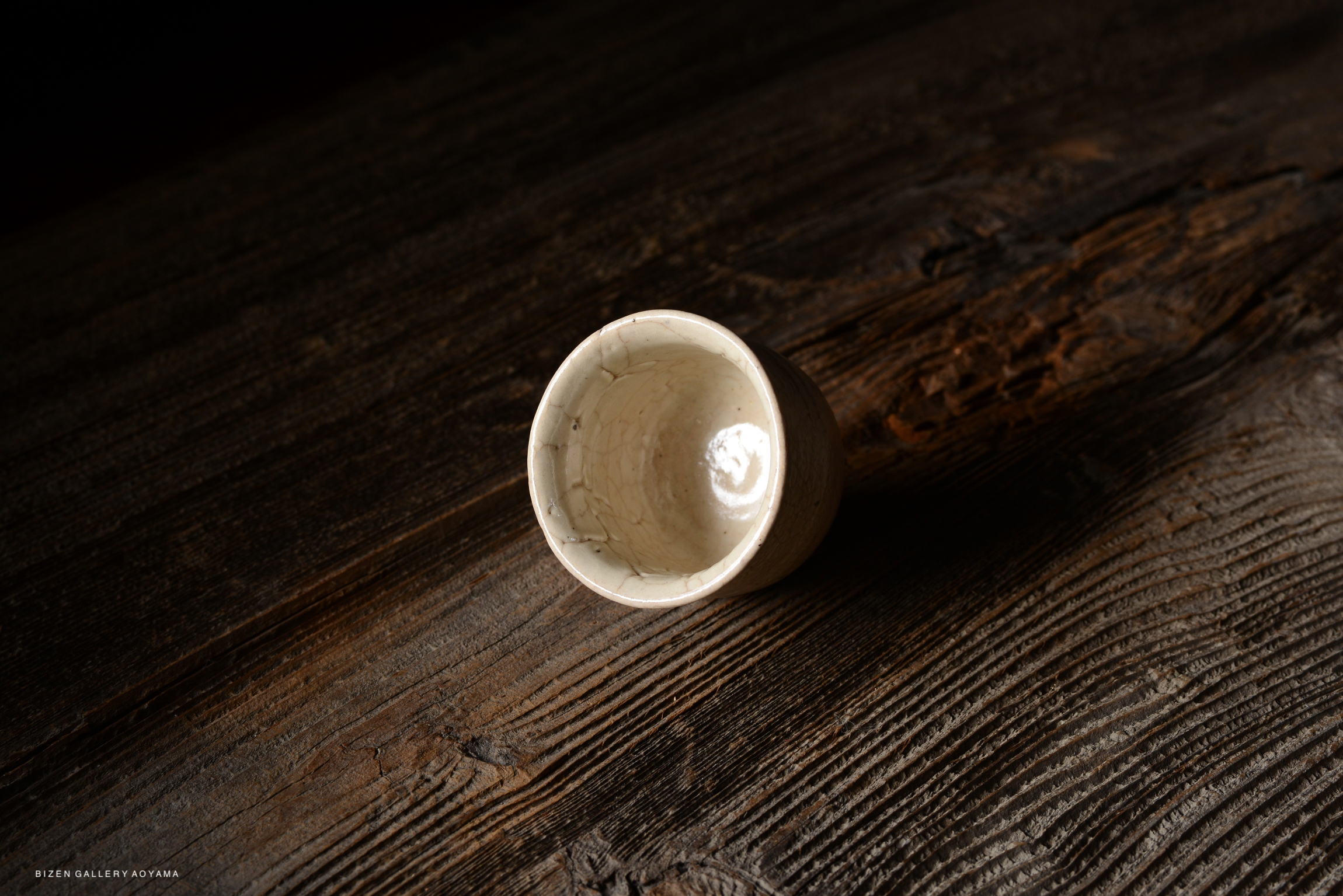 A close-up view of a small, crackled white ceramic cup placed on a textured wooden surface.