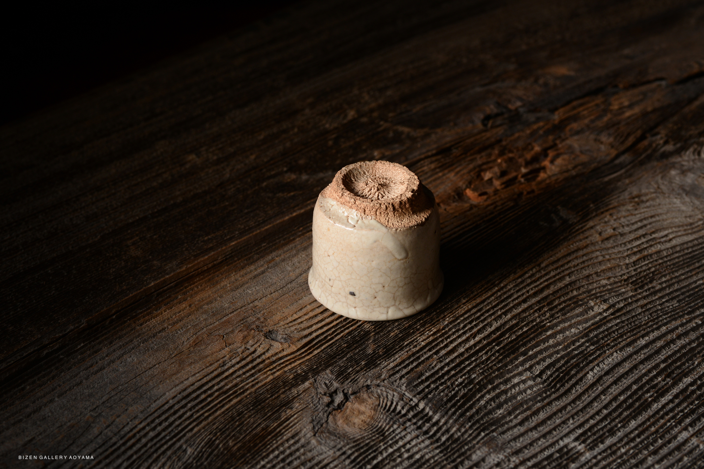 A small ceramic vessel with a textured top, resting on a wooden surface.