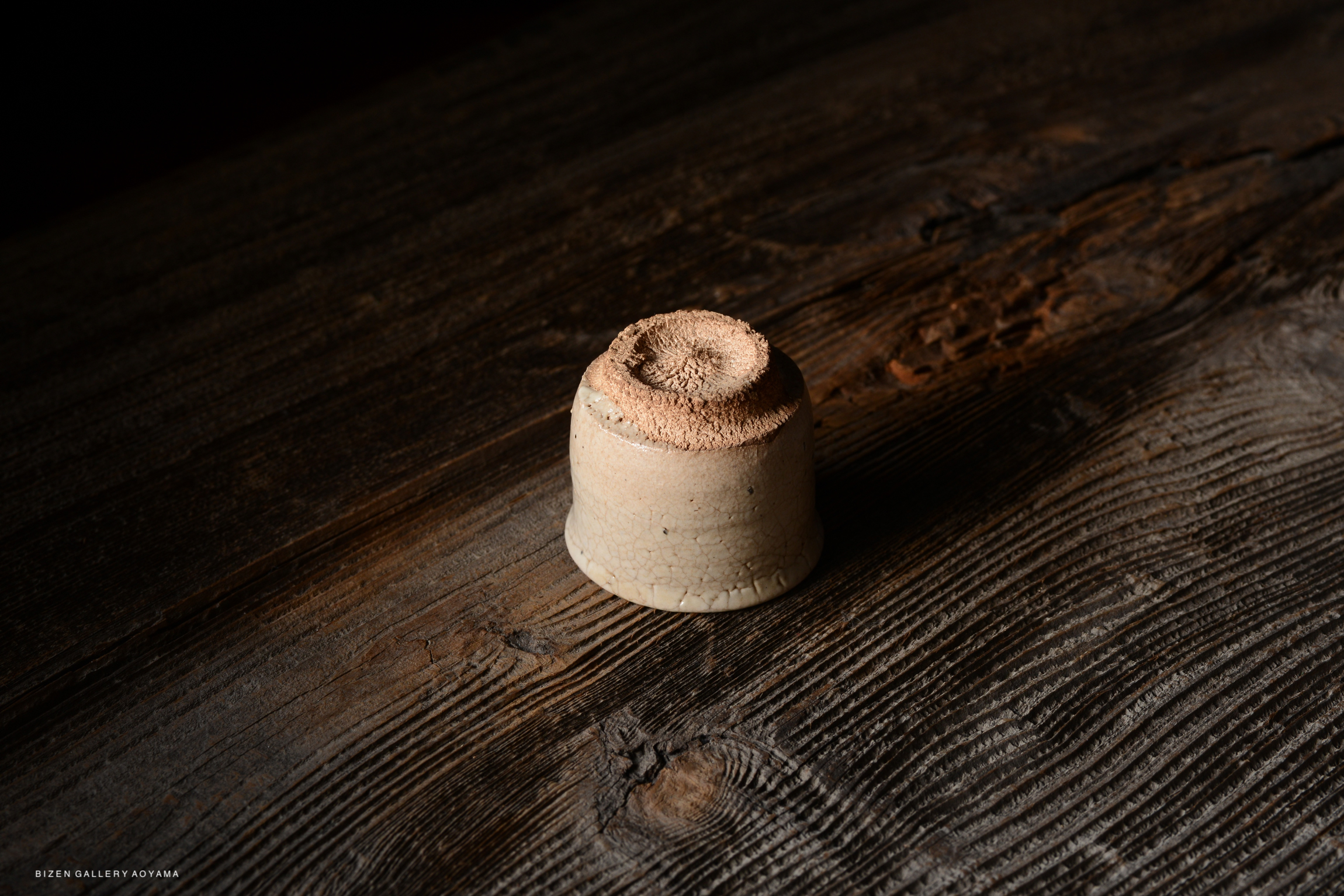 A close-up of a small ceramic piece with a textured top, resting on a wooden surface.