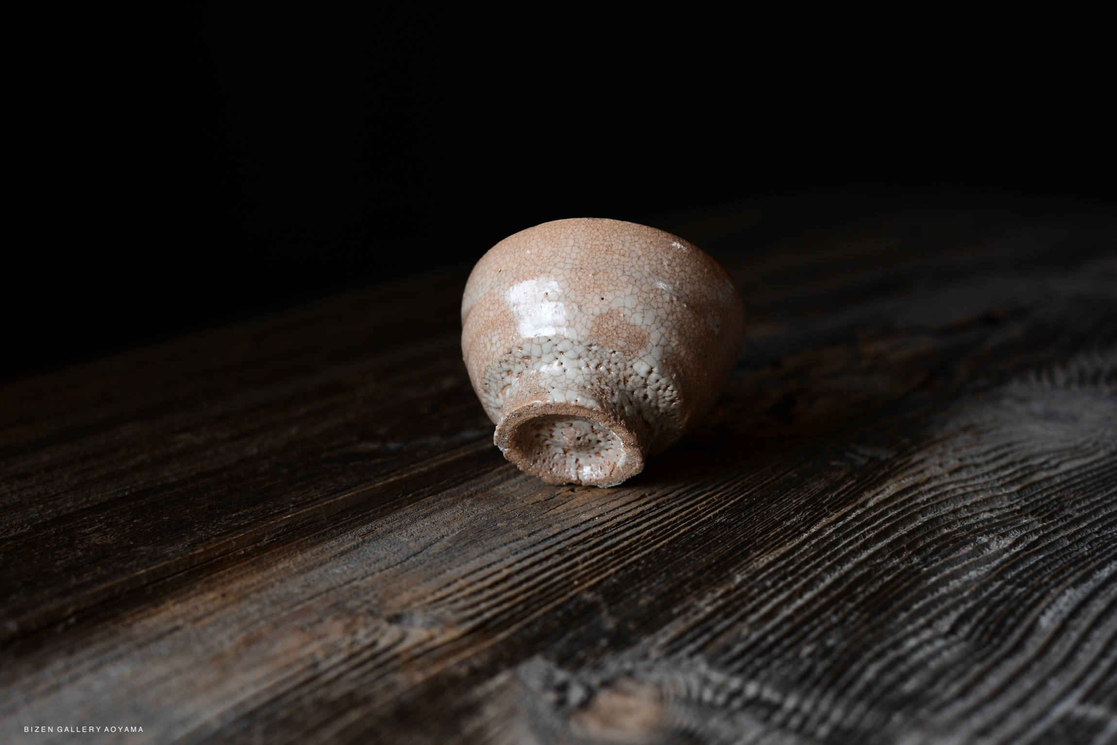 A close-up image of a textured ceramic bowl resting on a wooden surface, with a dark background.