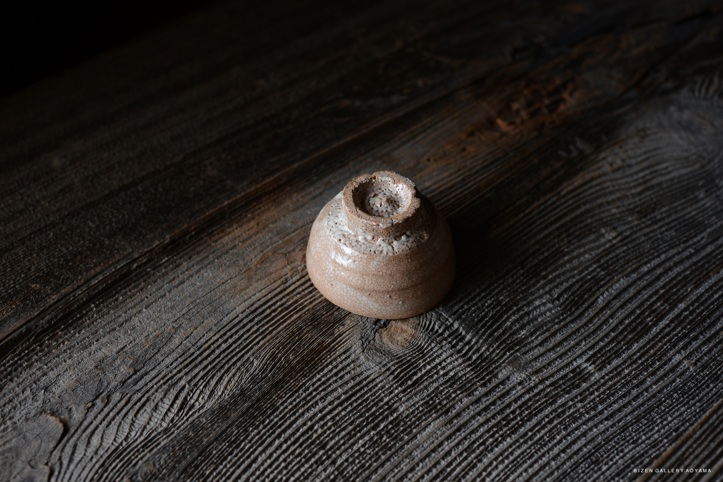 A small, elegantly crafted ceramic bowl with a textured surface, placed on a rustic wooden table.