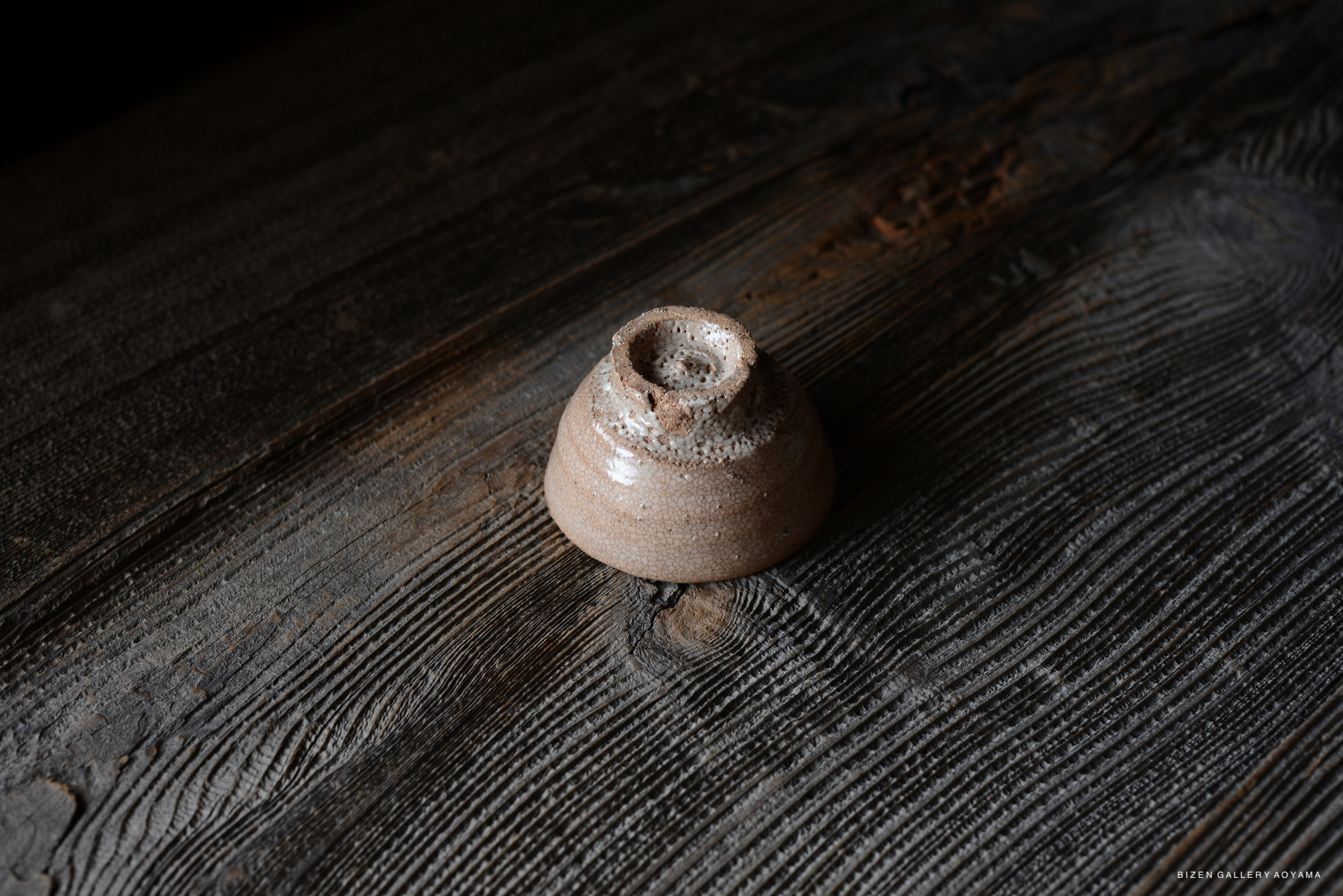 A close-up image of a handcrafted, earthy-toned pottery piece sitting on a textured wooden surface.