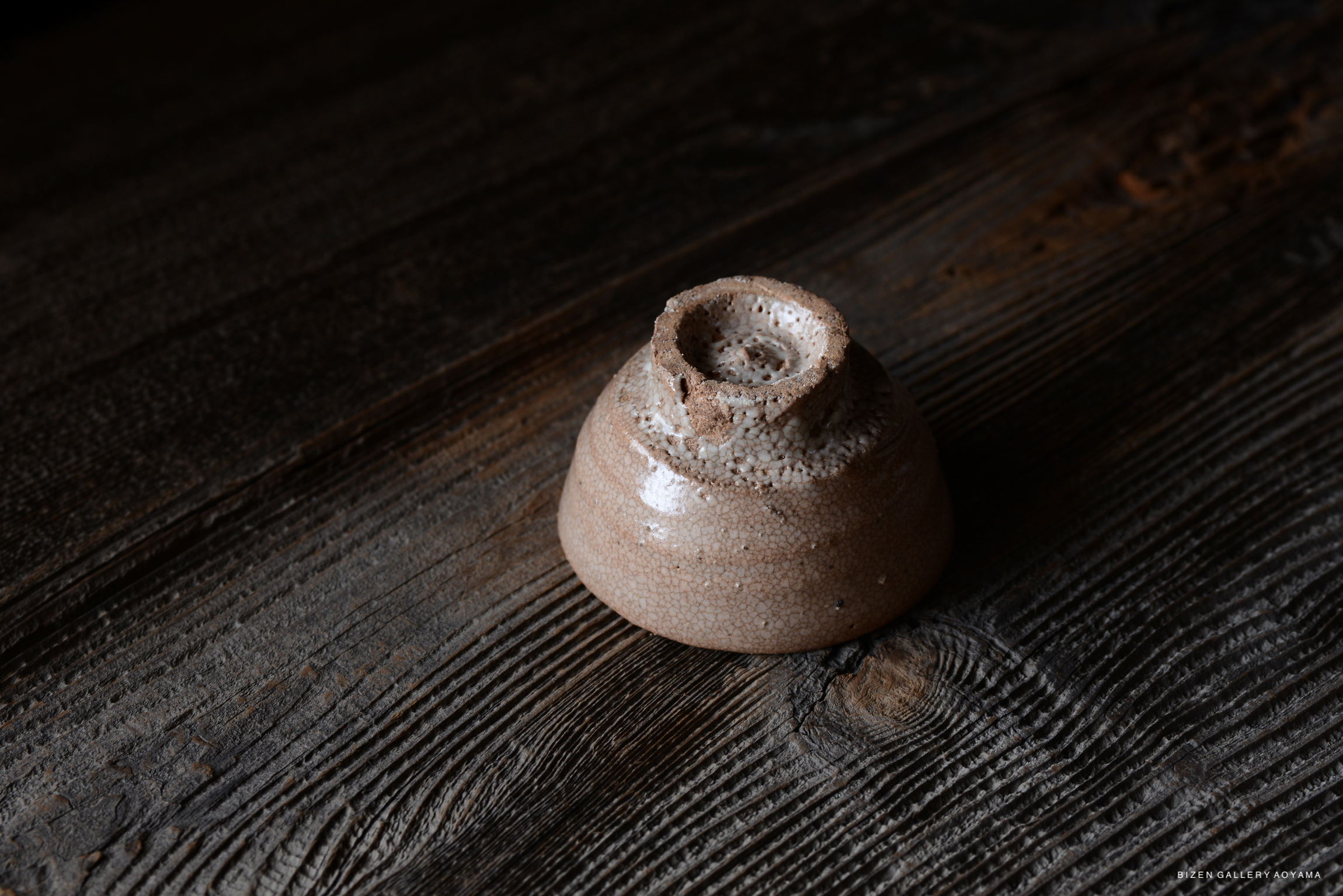 A rustic ceramic piece with a textured surface, displayed on a dark wooden table.
