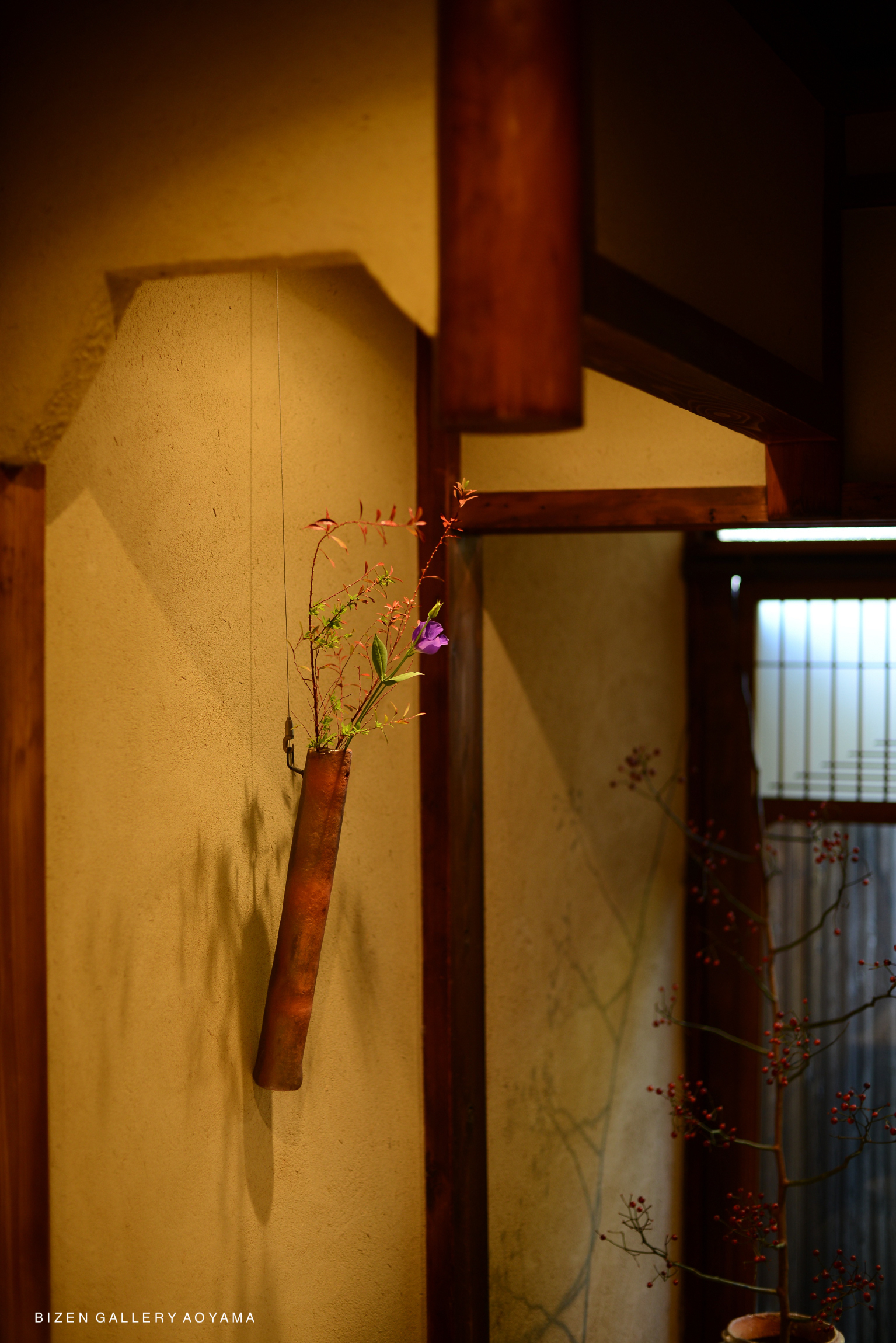 A hanging arrangement featuring delicate flowers in a rustic vase, with wooden beams and a textured wall background.