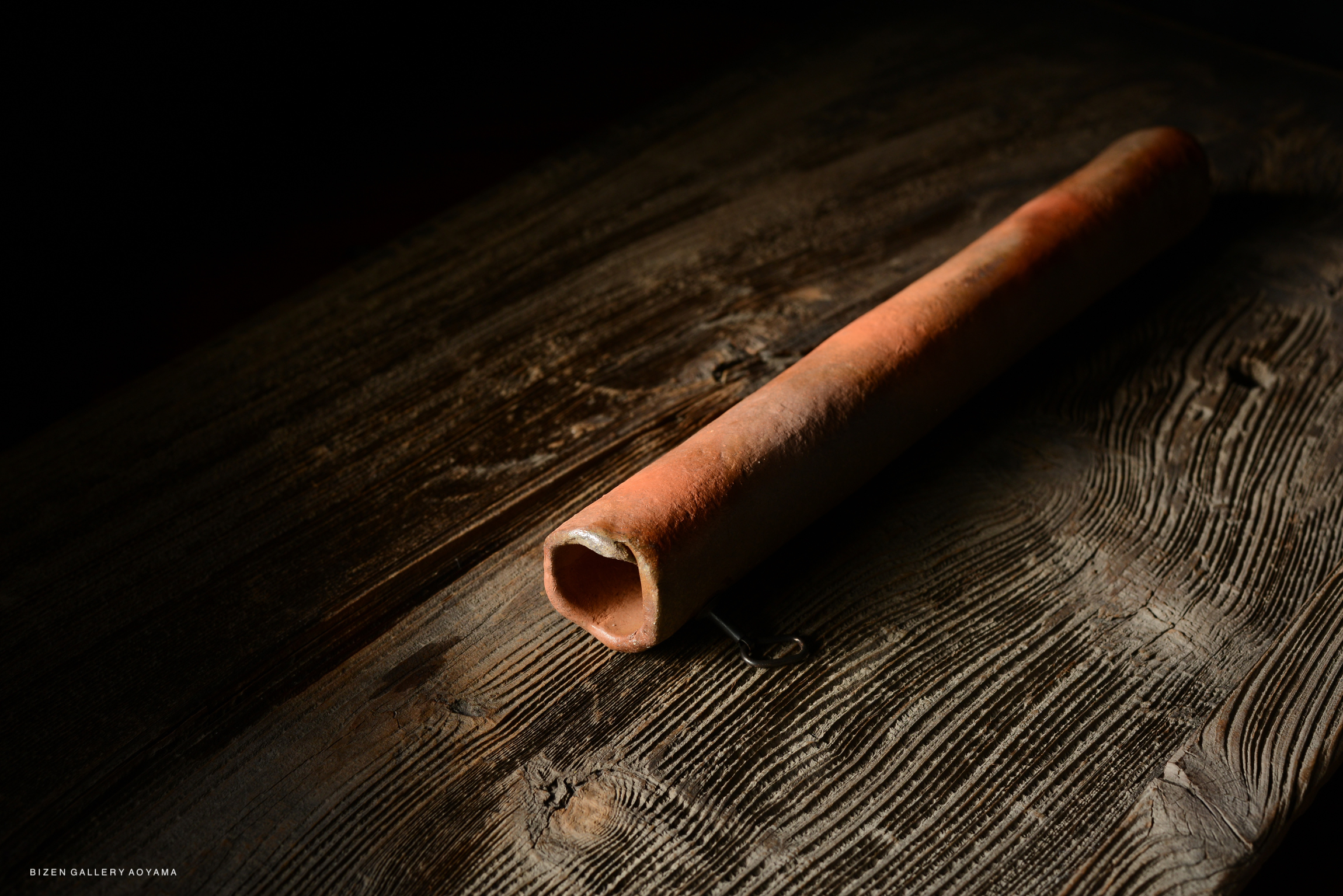 A Bizen kakehanaire, a traditional ceramic vase, placed on a wooden table with warm lighting.