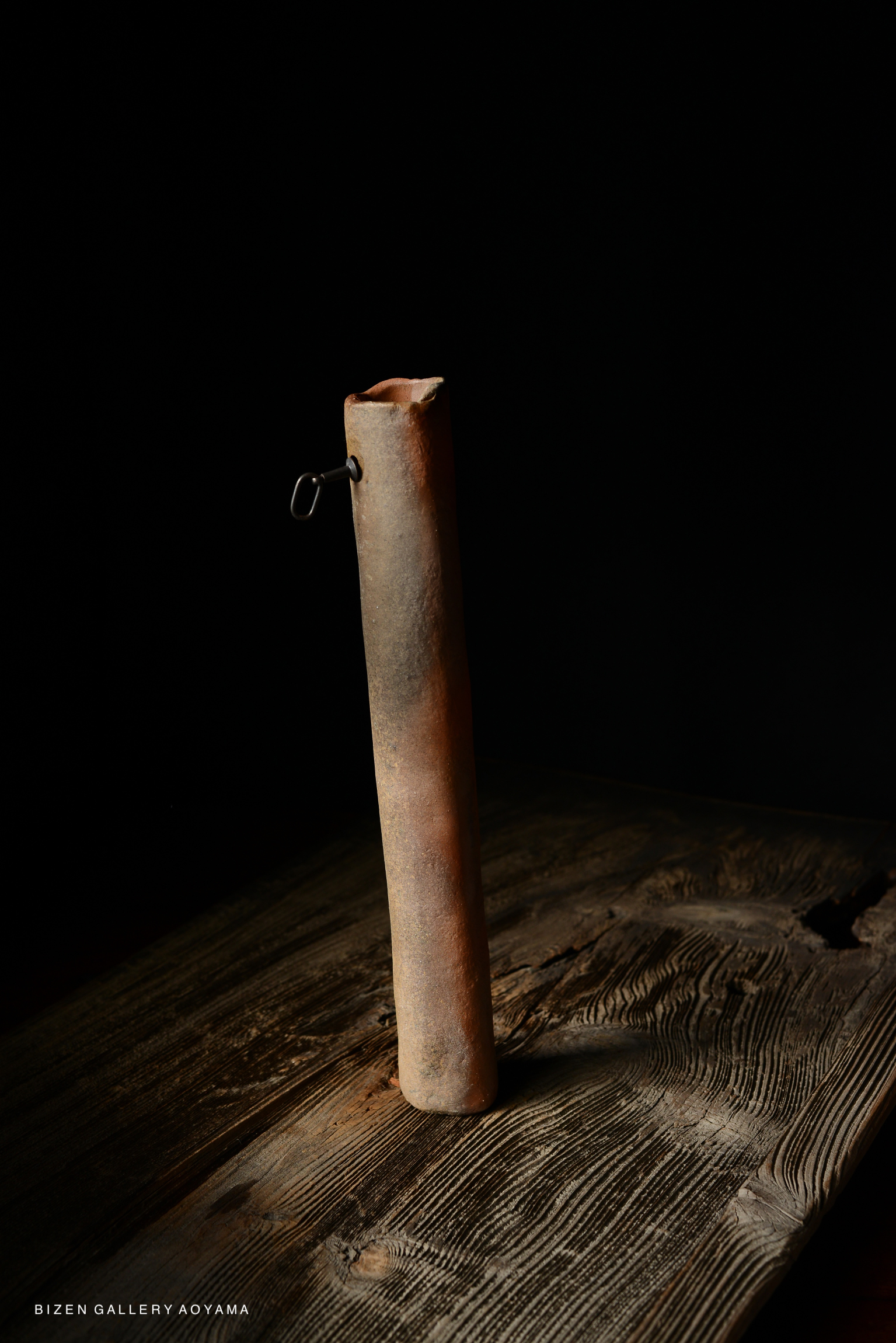 A Bizen ceramic vase with a rustic finish displayed against a dark background on a wooden surface.