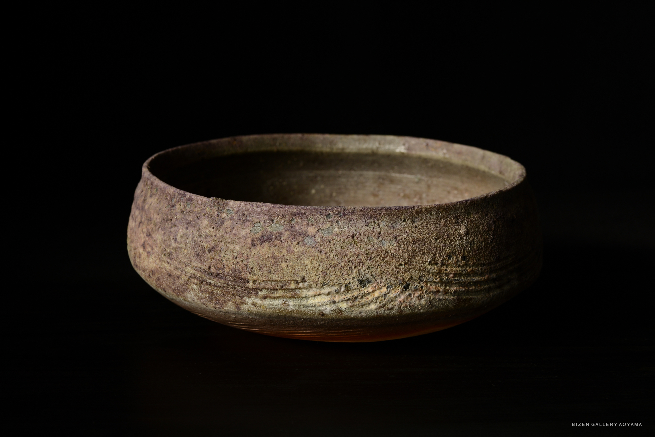 A close-up view of a textured ceramic bowl with a rustic finish, set against a dark background.