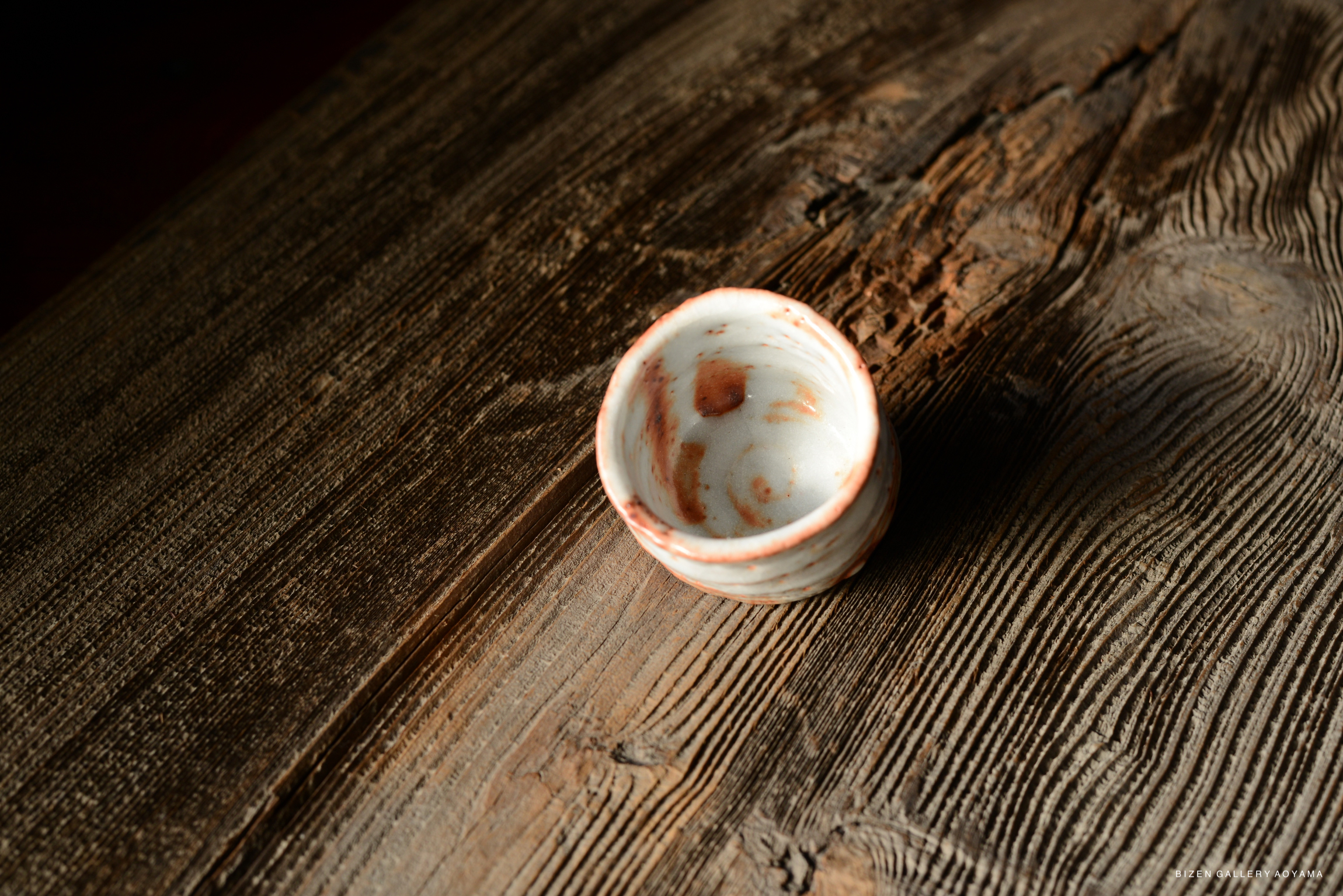 A small, round ceramic bowl with a speckled white and reddish-brown surface, resting on a rustic wooden table.