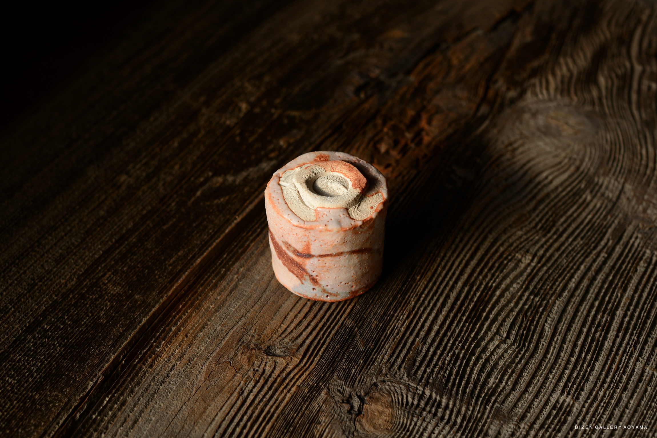 A Shino Guinomi sake cup with a unique design, displayed on a rustic wooden surface.