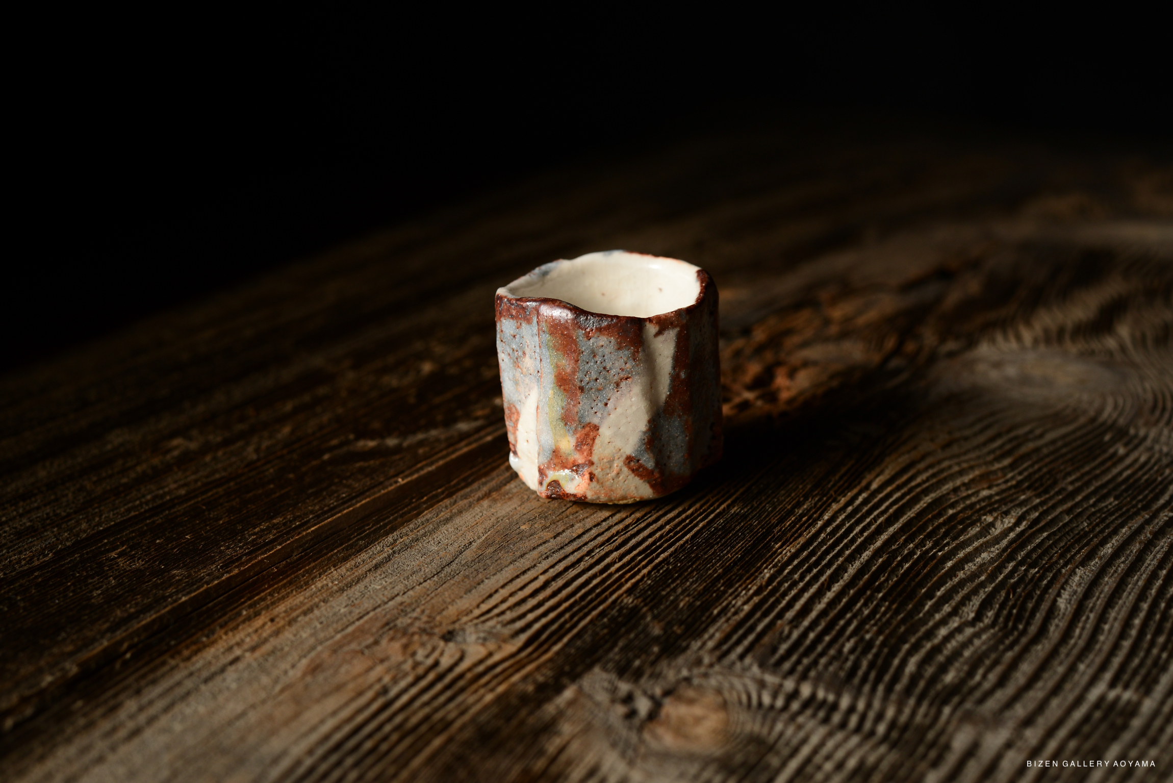 A handcrafted Shino guinomi, characterized by its unique texture and color variations, resting on a wooden surface.