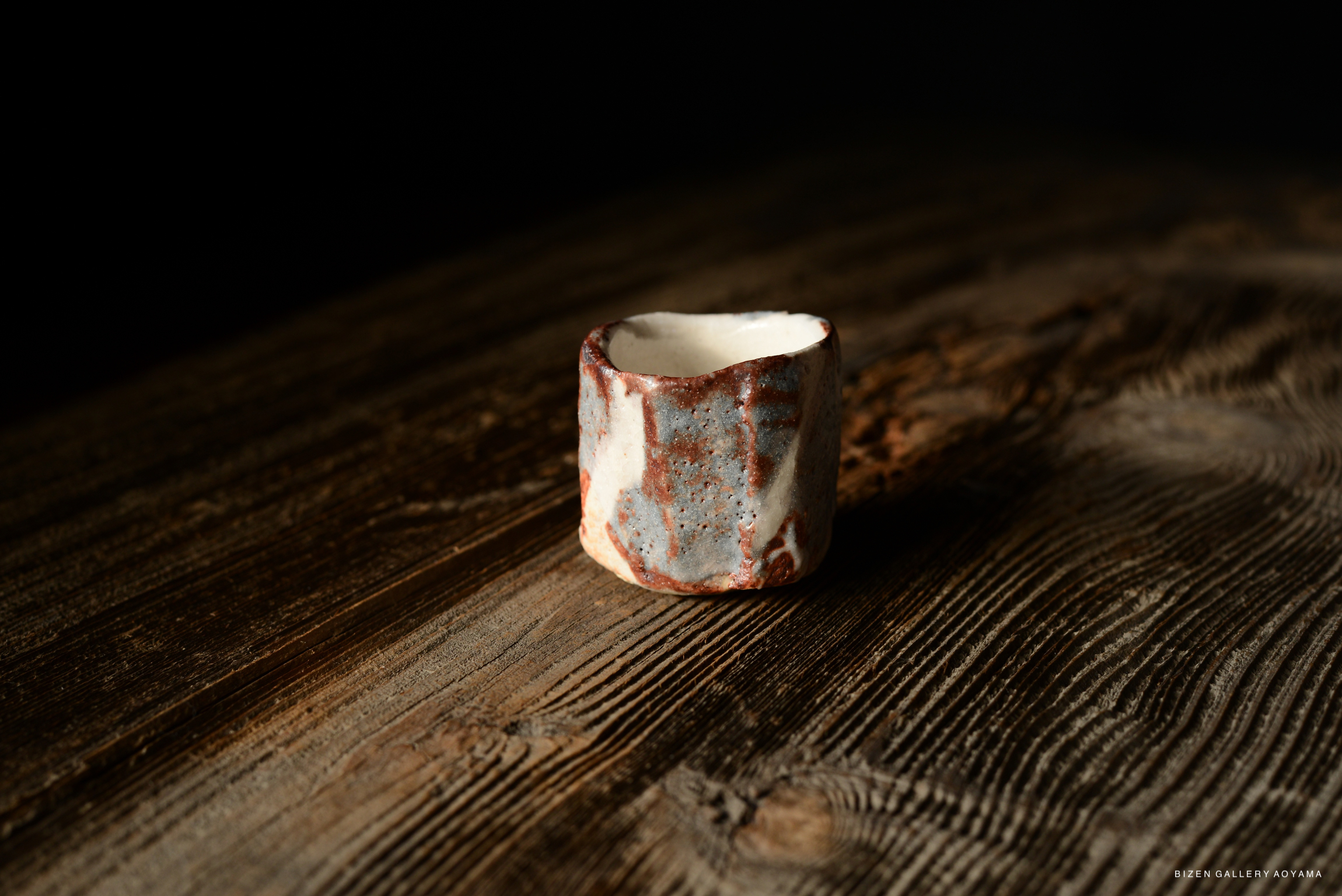 A Shino Guinomi ceramic sake cup with a distinct textured surface, displayed on a wooden table.