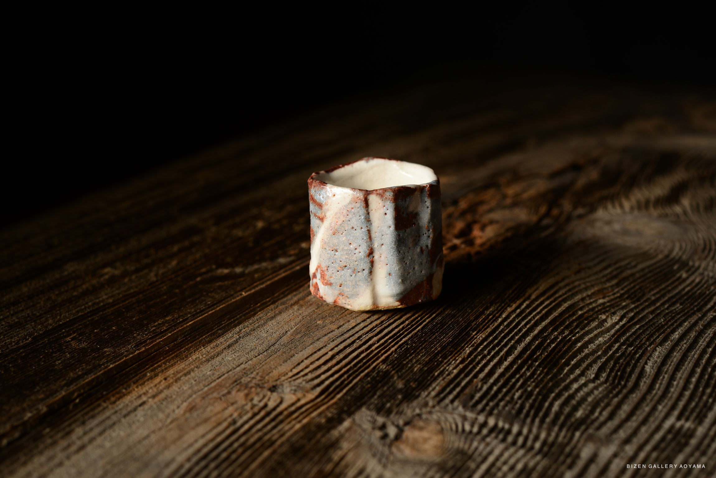 Shino Guinomi sake cup with a textured surface, featuring earthy tones of white and reddish-brown, set on a wooden surface.