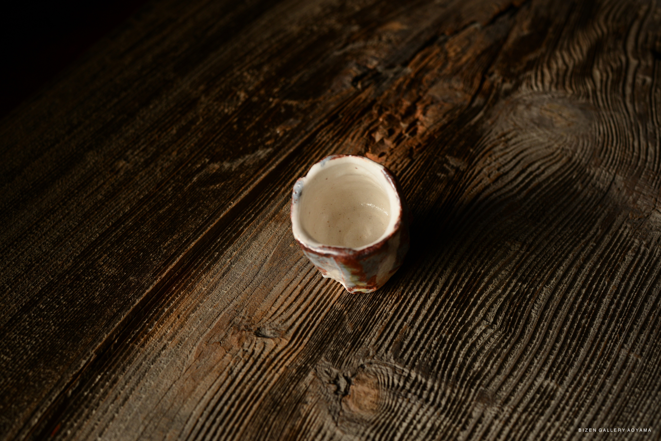 A close-up view of a Shino Guinomi sake cup resting on a wooden surface, showcasing its unique texture and color.