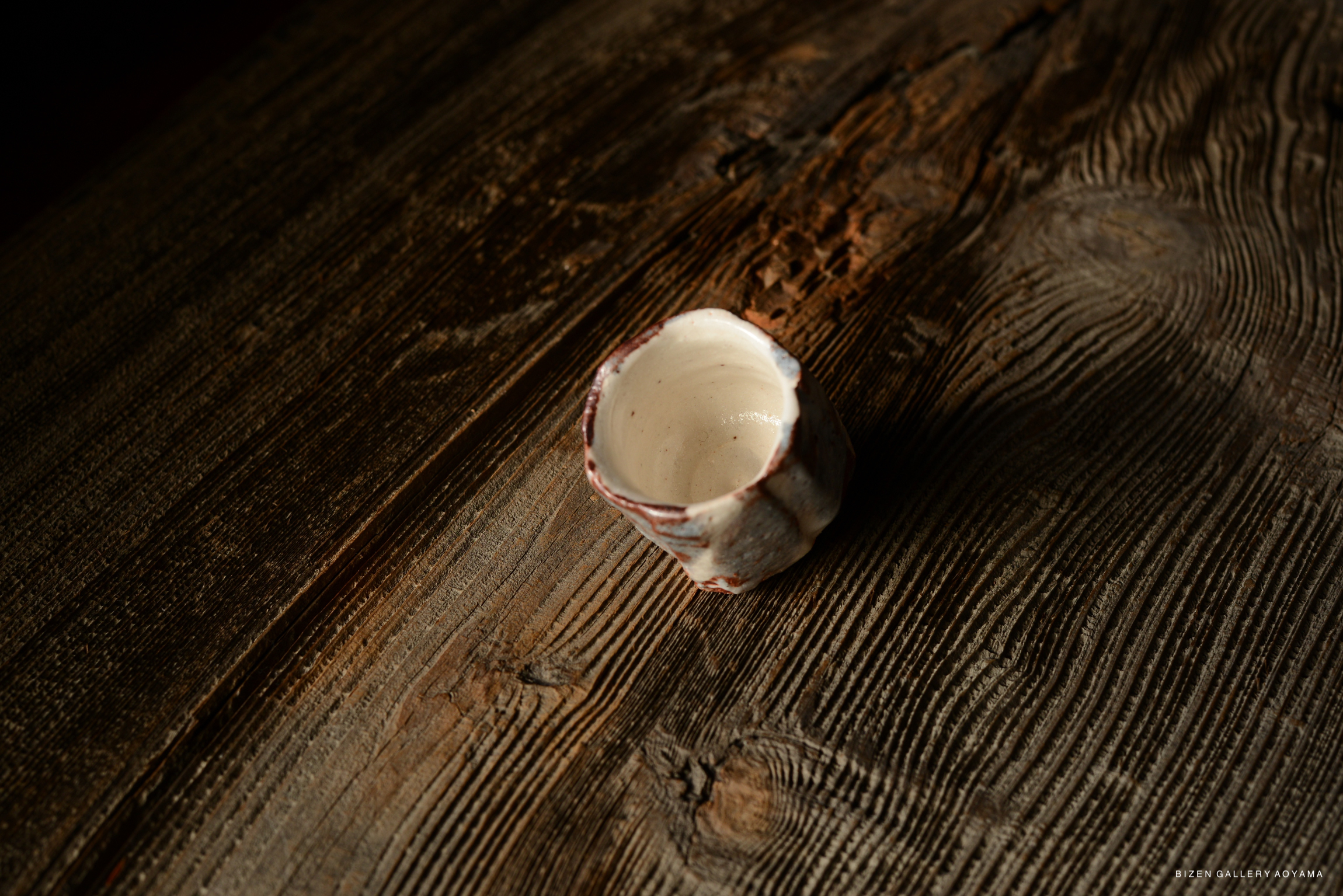 A handcrafted Shino guinomi sake cup with a unique texture and design, set on a rustic wooden surface.