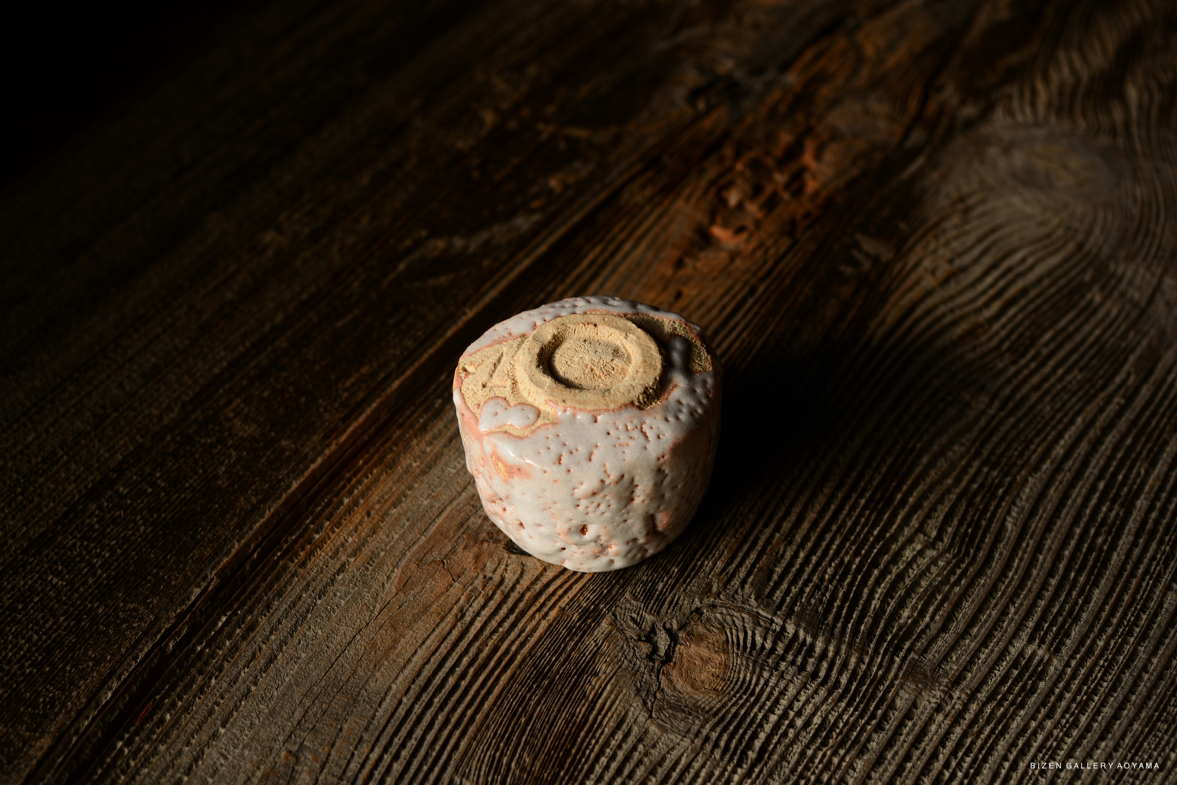 A close-up view of a Shino ceramic sake cup with a textured surface, displayed on a rustic wooden background.