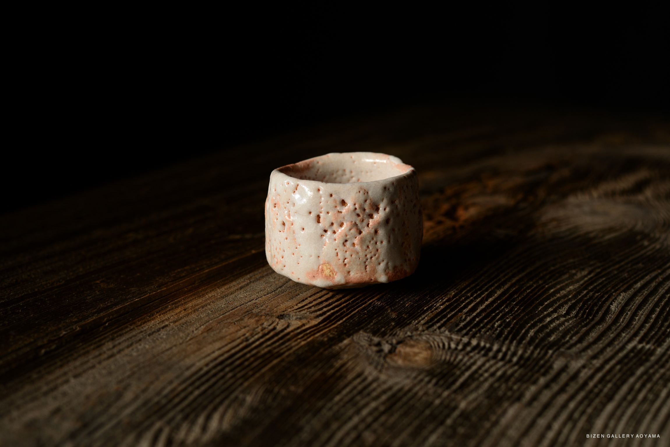 A Shino Guinomi sake cup with a textured, speckled surface, displayed on a wooden table.