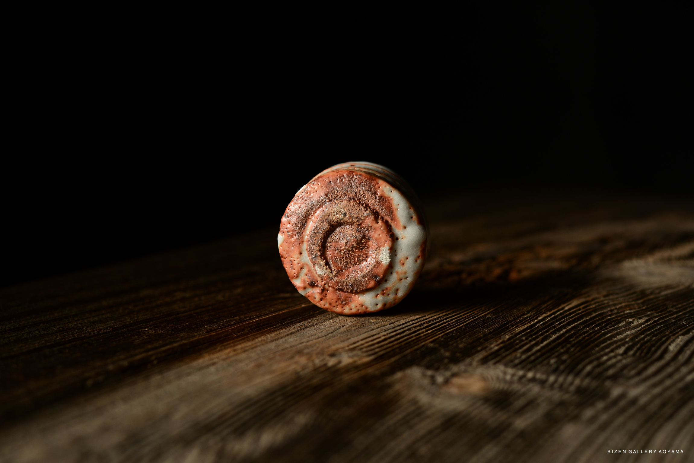 Close-up view of the bottom of a ceramic piece, featuring a textured design and earthy tones, positioned on a wooden surface.