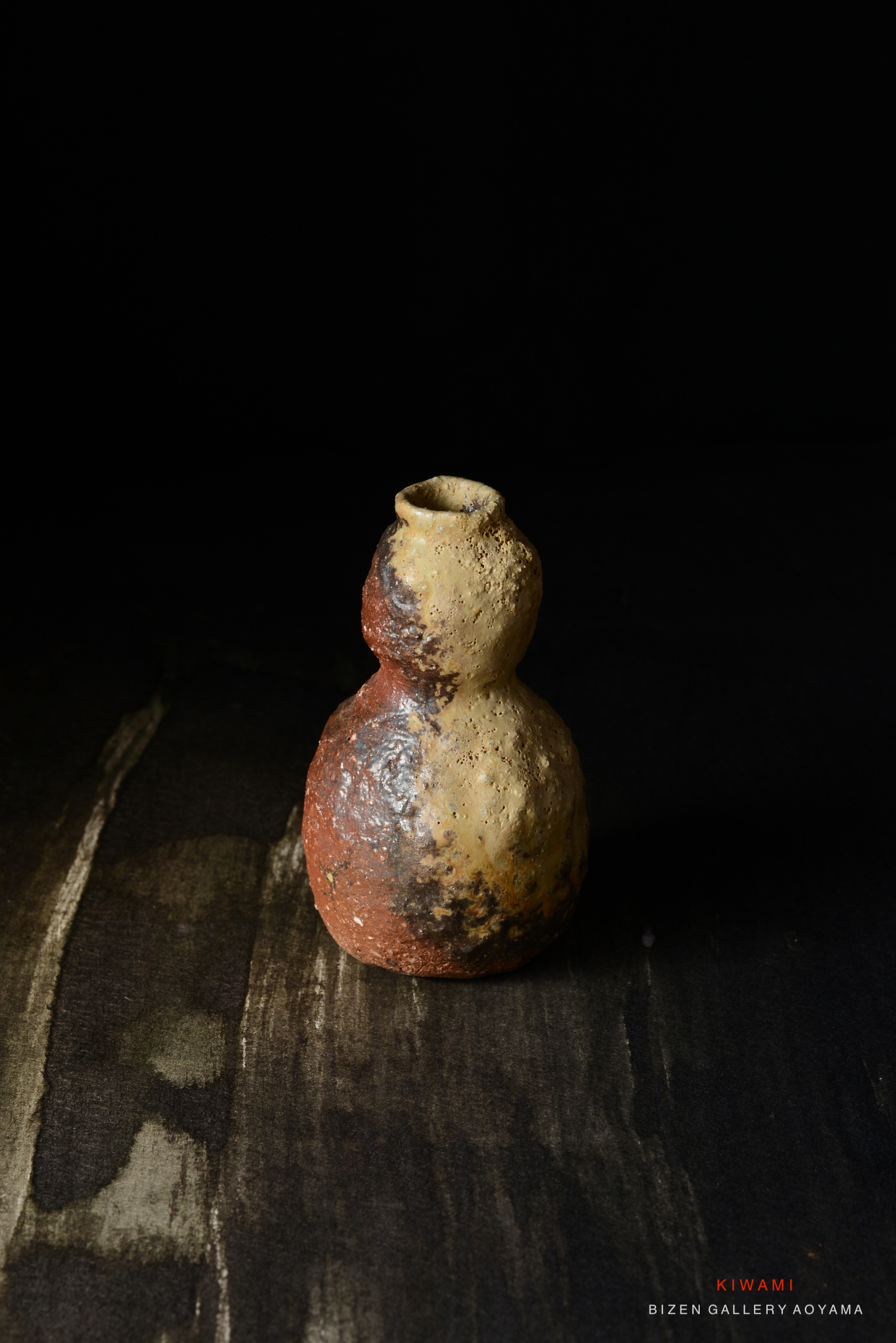 黒い背景に置かれた陶器の花瓶。丸みを帯びた形状で、オレンジ色と黄色の斑点が特徴的。