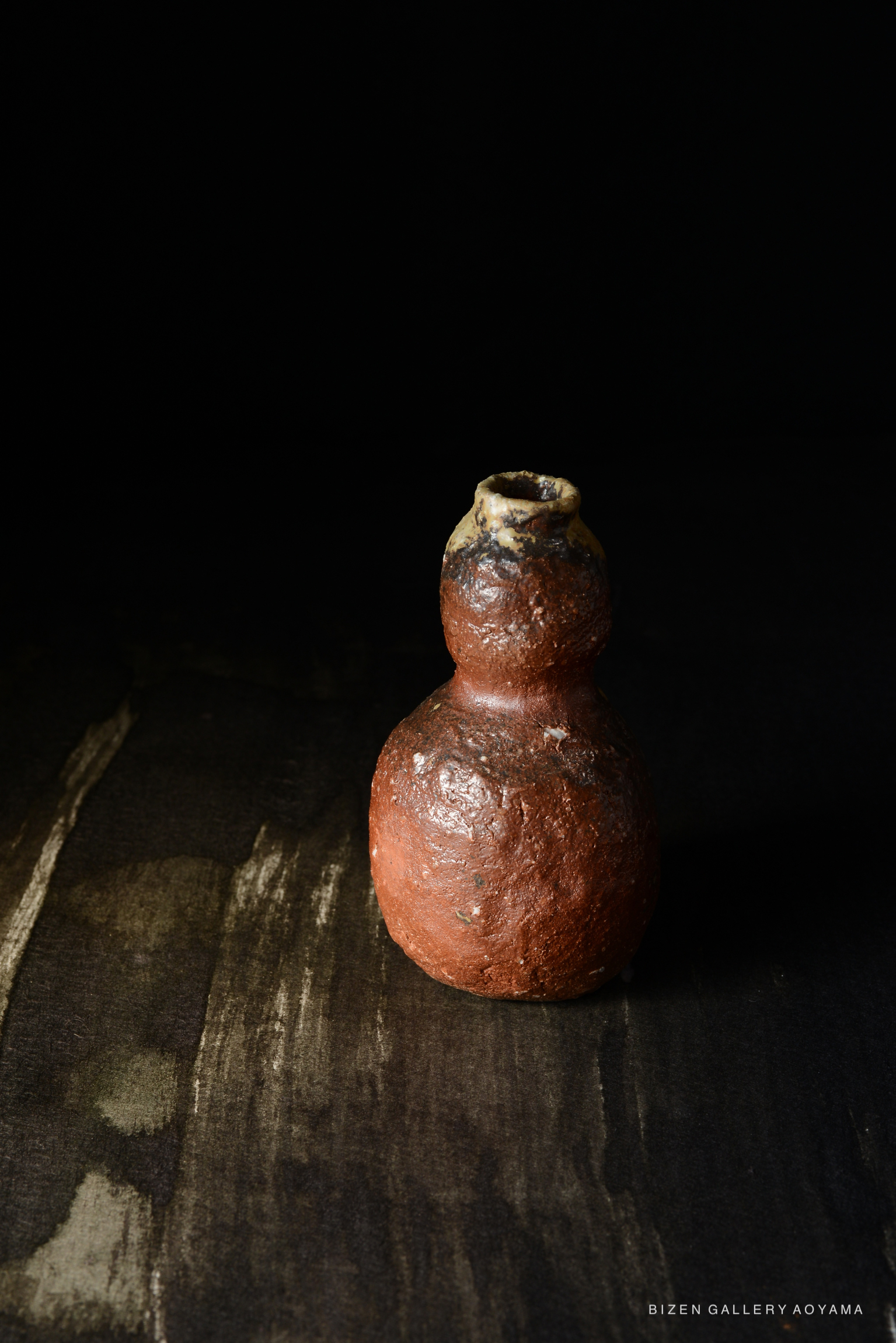 黒い背景の前に置かれた赤茶色の陶器の瓶