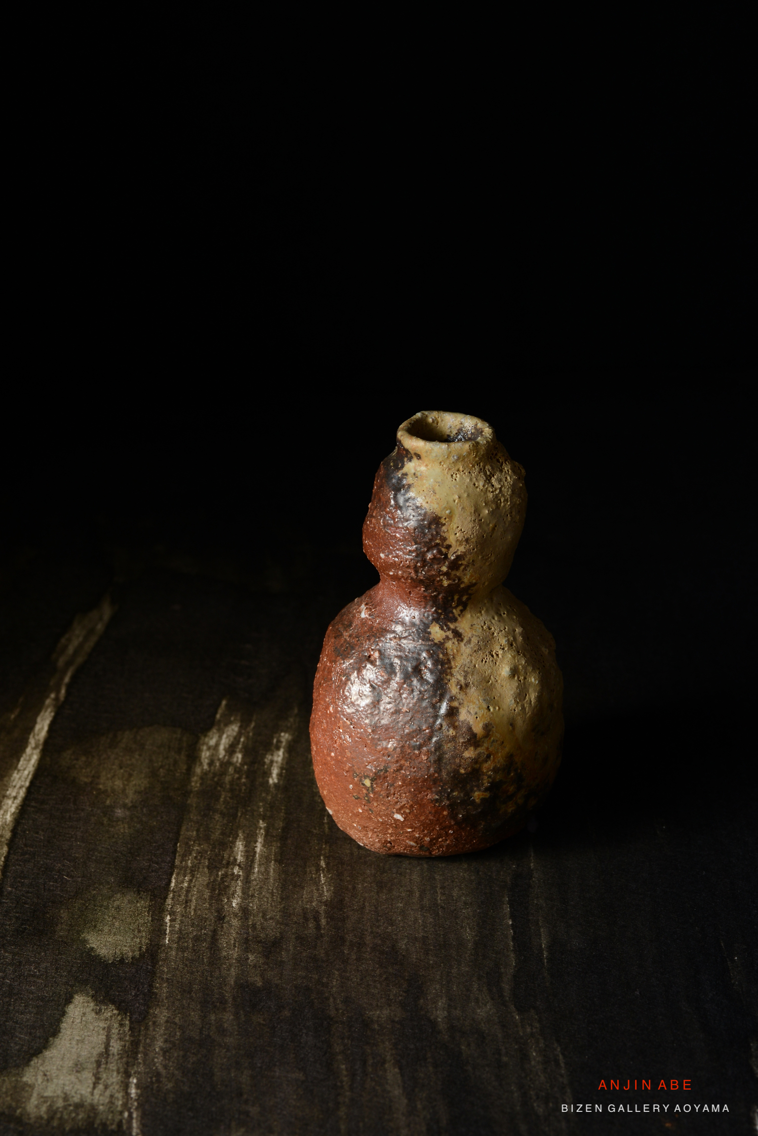 黒い背景の前に置かれた、独特の形状と色合いを持つ陶器の壺