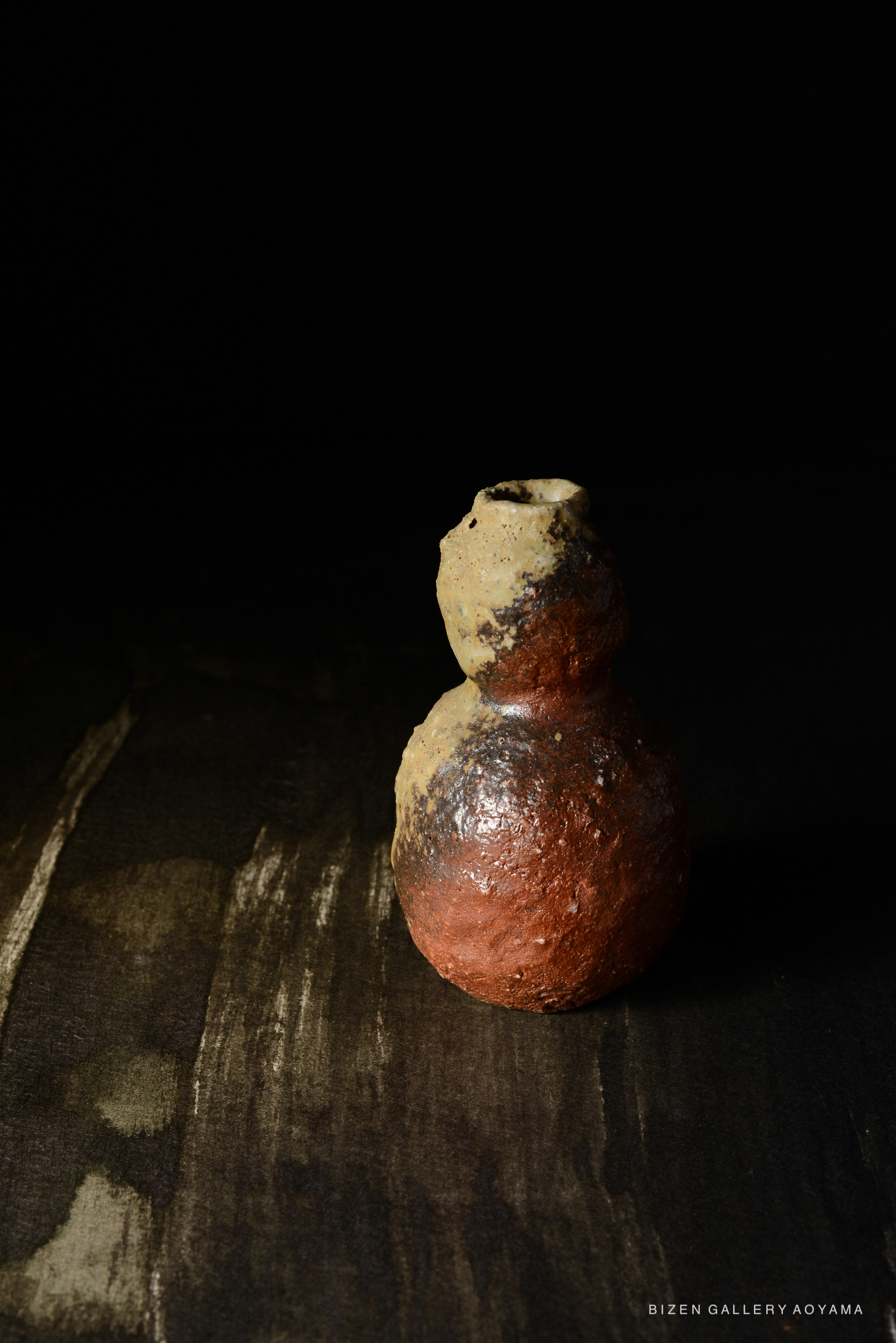 黒い背景の前に置かれた、茶色とベージュの色合いを持つ独特な形の陶器