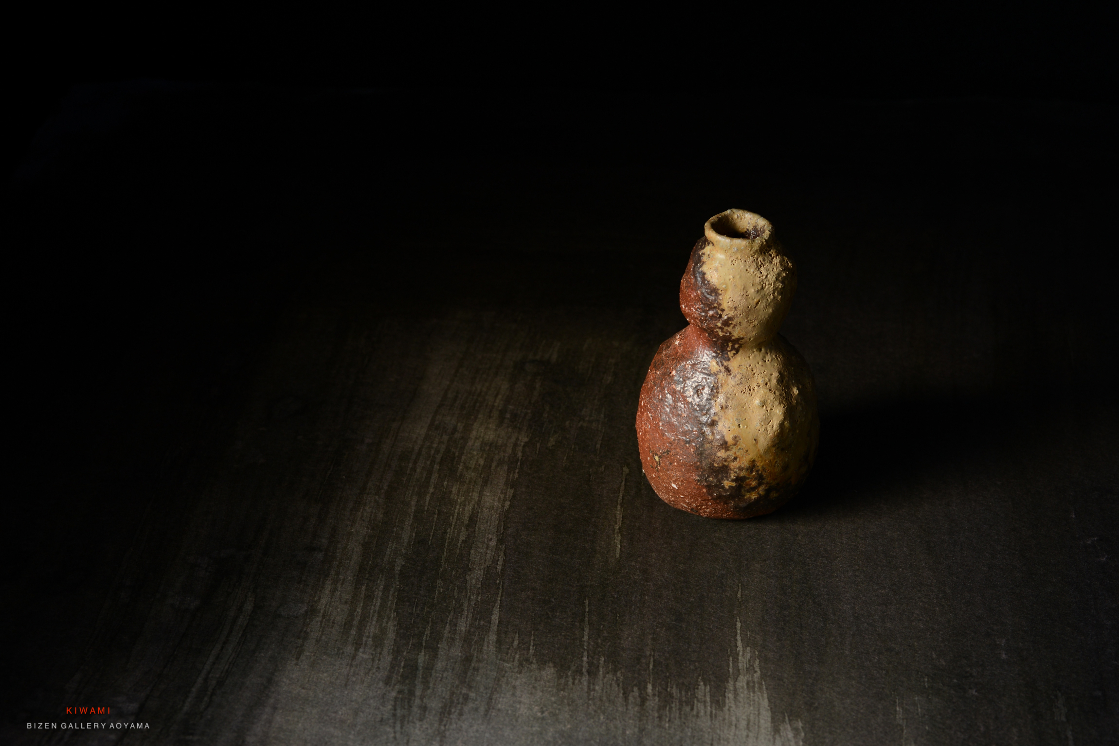 黒い背景の上に置かれた、独特な形状の陶器の花瓶。赤と黄色の斑点があり、自然な質感を持つ。